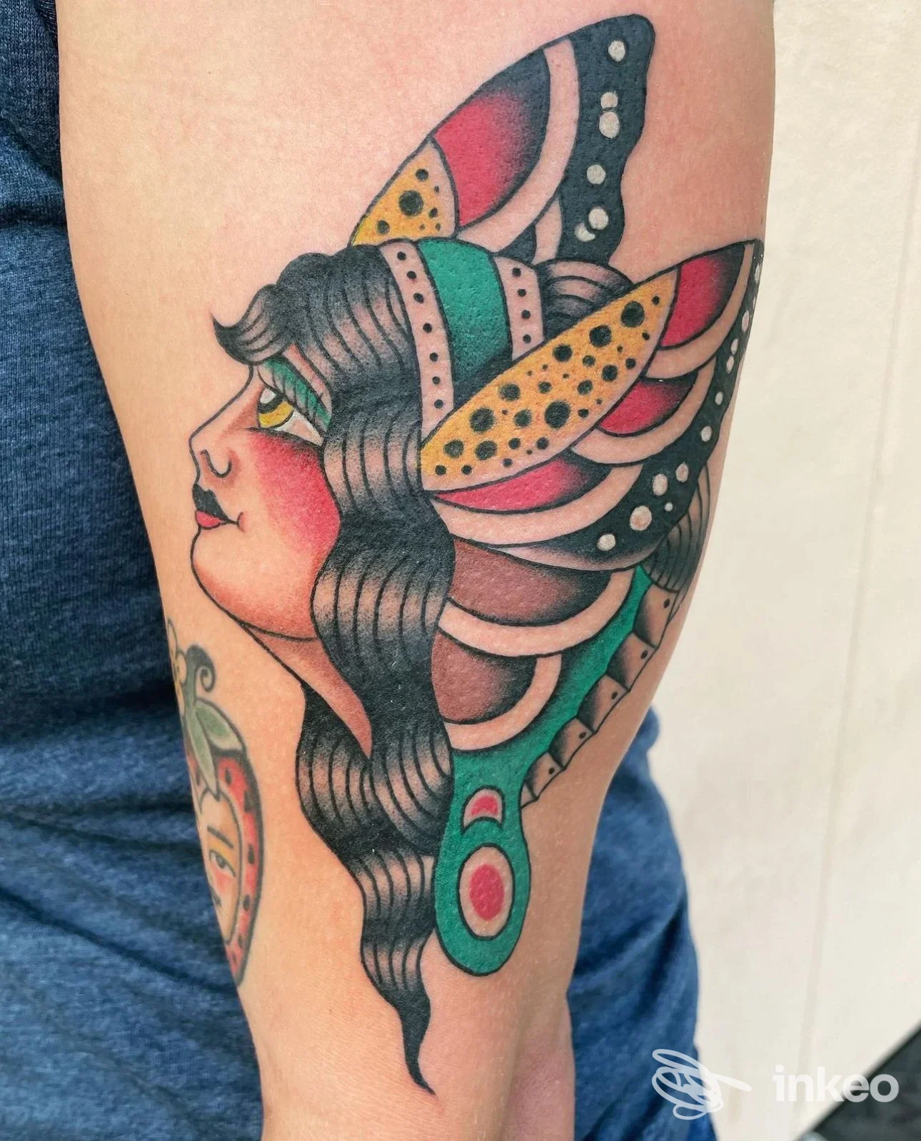 Tatuaggio colorato in stile tradizionale/neo-tradizionale raffigurante il profilo di una donna con elementi a farfalla sull'avambraccio, Hands Across the Sea Tattoo Parlour, Olbia.