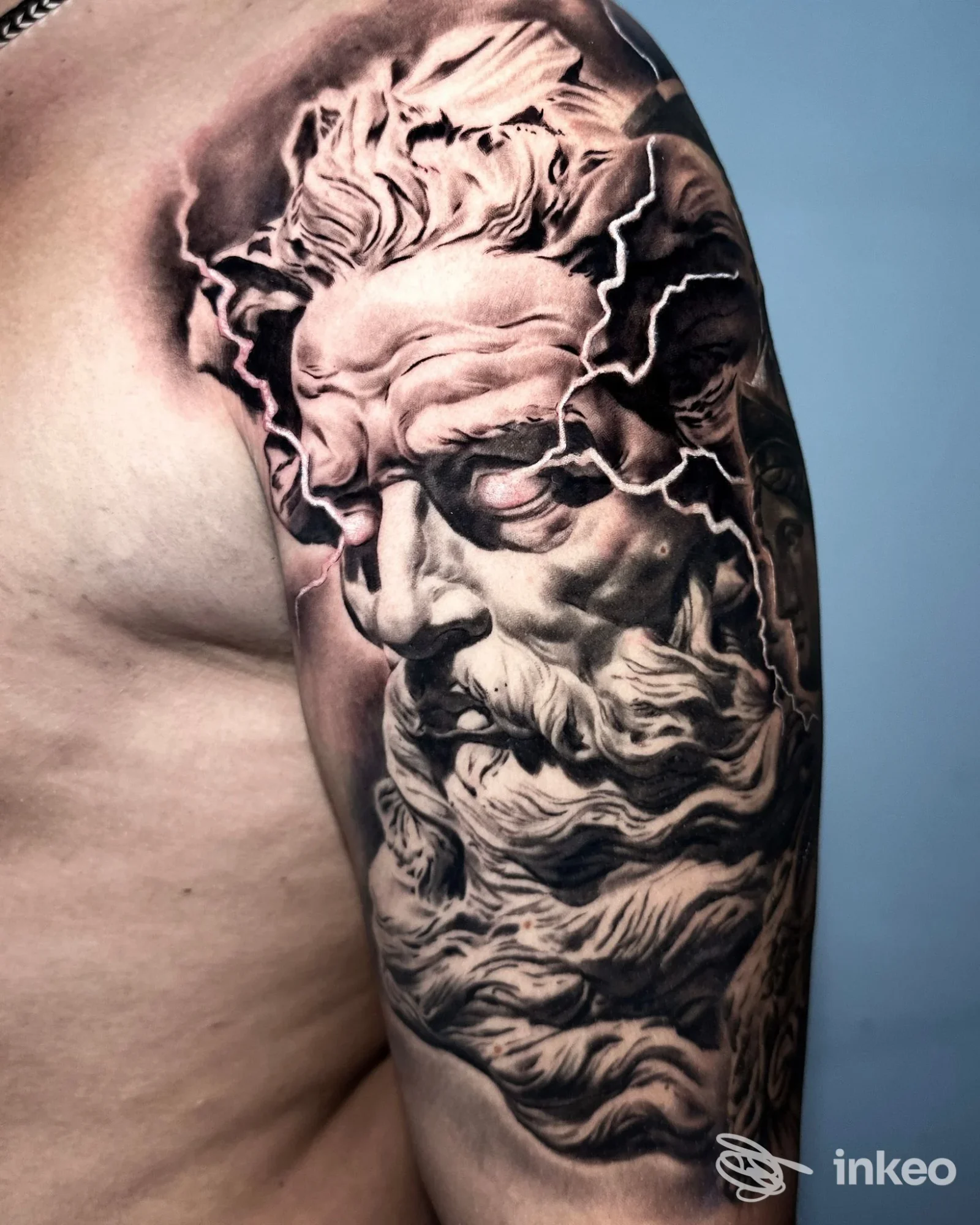 Tatuaggio realistico in bianco e nero su braccio e spalla, ritratto con barba e fulmini — Revolver Tattoo Studio, Oristano.