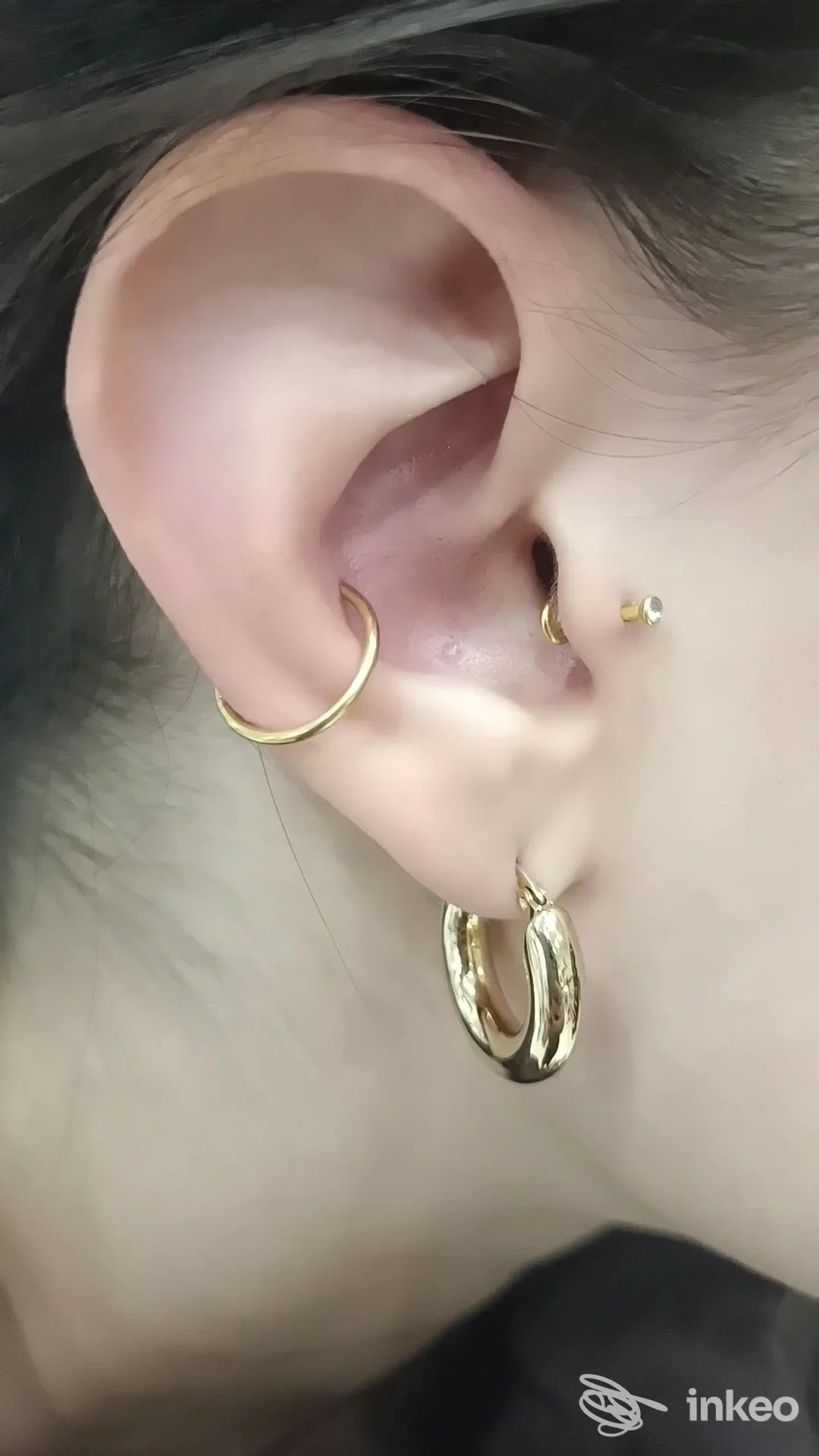 Primo piano di un orecchio con tre piercing dorati. Piercing & Beauty Center, Firenze.