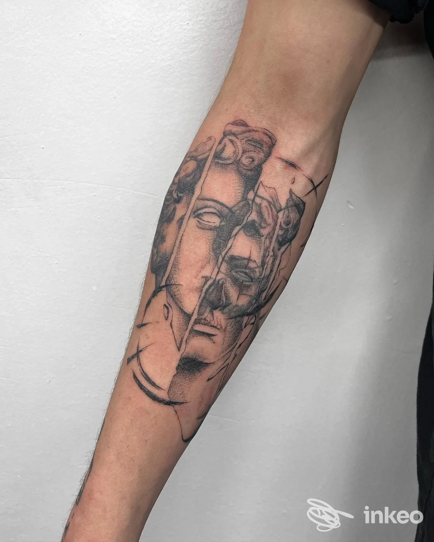 Tatuaggio in bianco e nero sull'avambraccio con volti frammentati e segni grafici, foto fornita da Lema Tattoo, Iglesias.