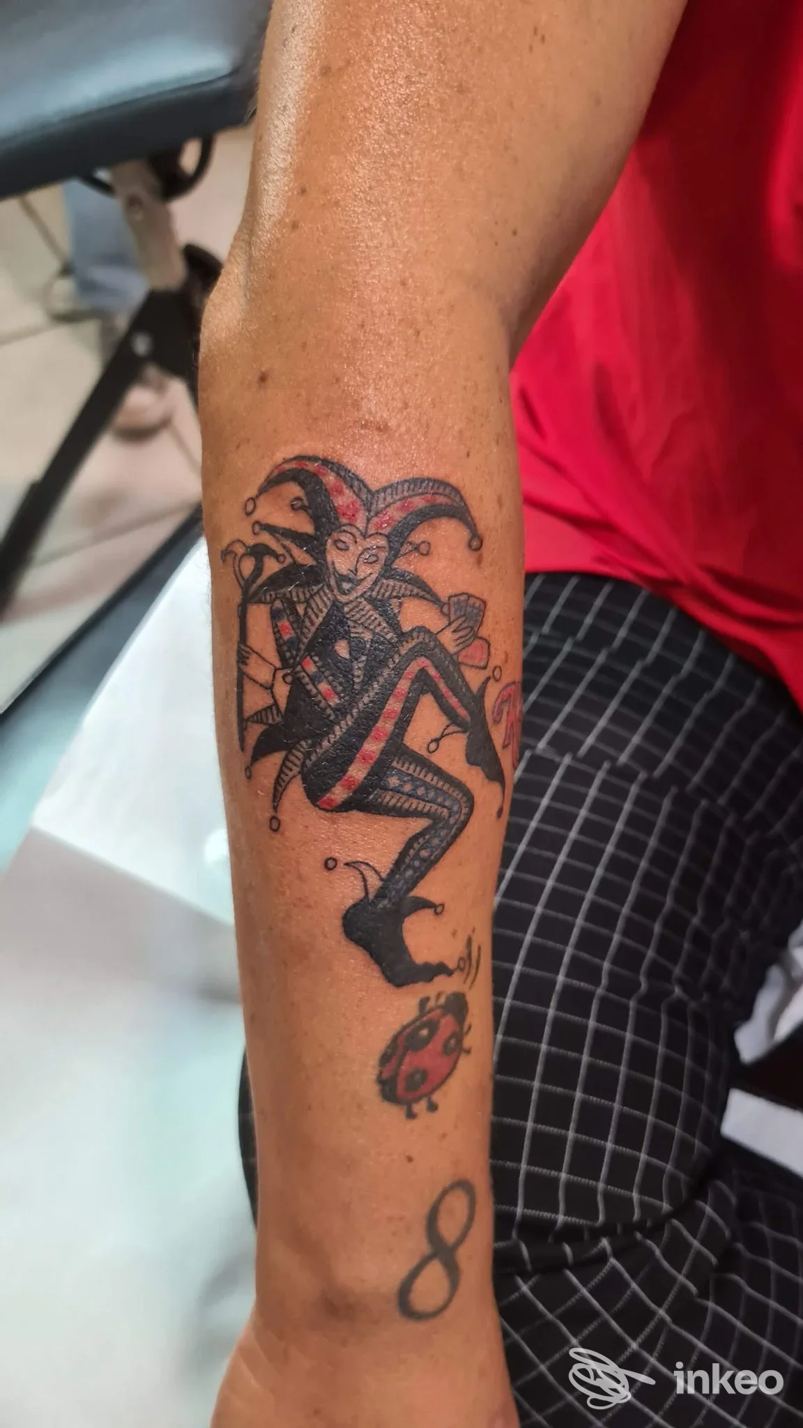 Avambraccio con tatuaggio di giullare in stile tradizionale, più coccinella e cifra otto, foto da Hard Color Tatoo a Massa.