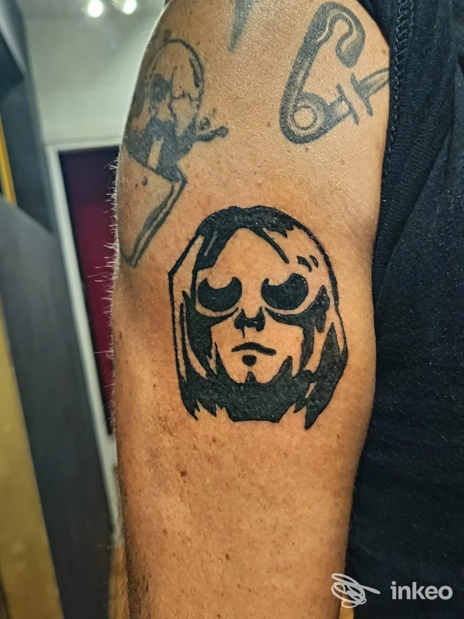 Primo piano del braccio con tatuaggio blackwork stilizzato di volto e altri piccoli tatuaggi; immagine da Eva Ink Black, Bolzano.