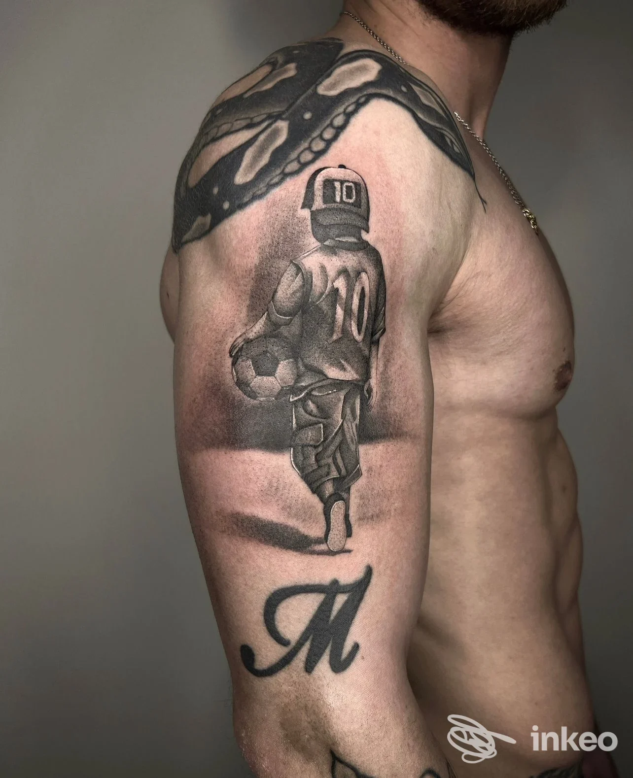 Tattoo realistico sull'avambraccio di un uomo, raffigurante un portiere di calcio, con una grande lettera M sul basso braccio; braccio nudo visibile, stile in chiaro scuro.