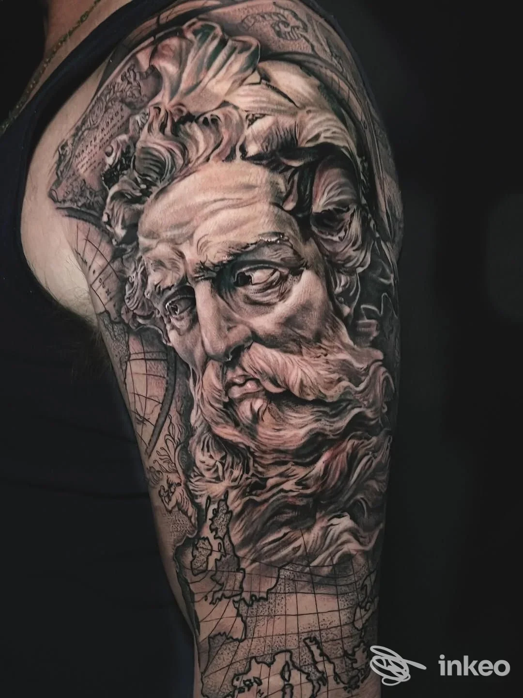 Grande tatuaggio realistico in bianco e nero sul braccio con volto classico e mappa, THTINK LAB, Riva del Garda.