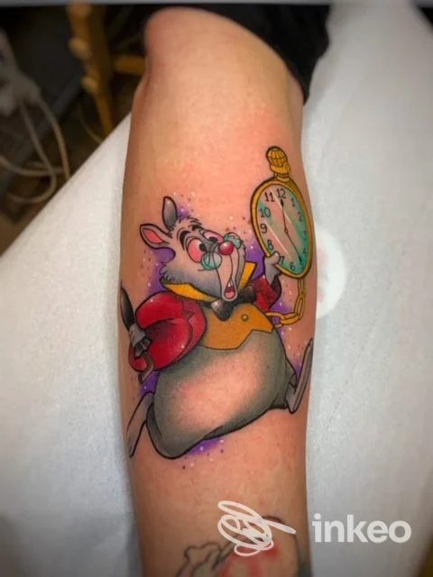 Tatuaggio colorato su braccio: un topo felice che regge un orologio da tasca, disegnato in stile fumetto.