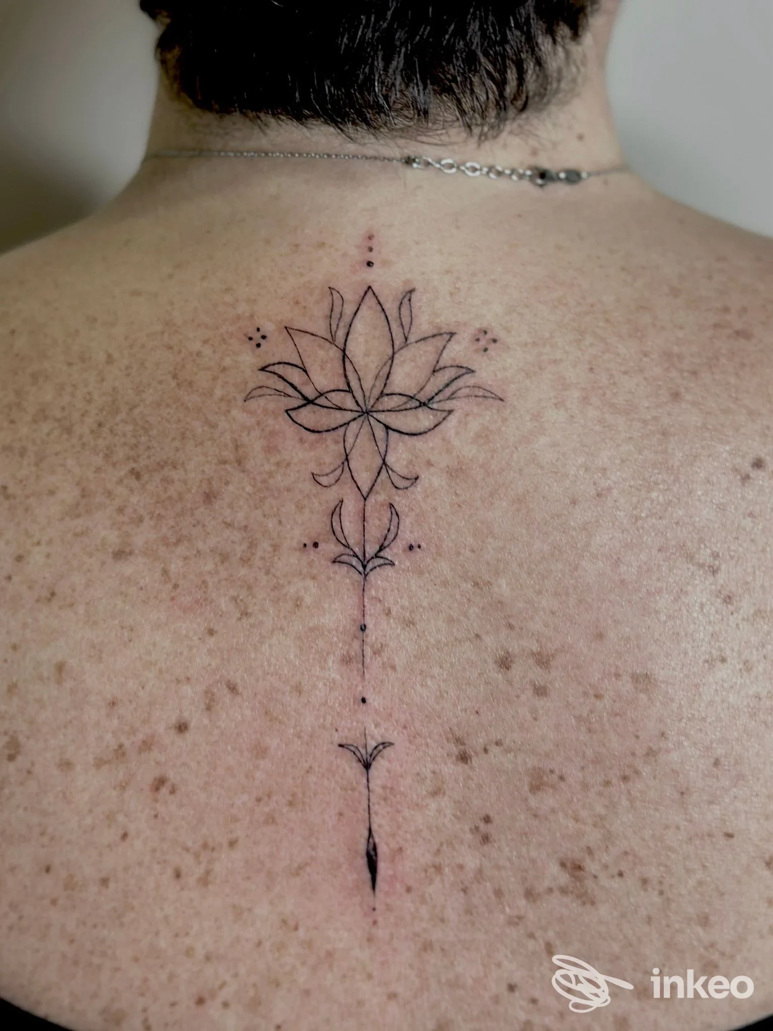 Tatuaggio linea sottile con loto lungo la colonna sulla parte superiore della schiena. Immagine per Ink Couture di Martina Teolato, Maserà di Padova.