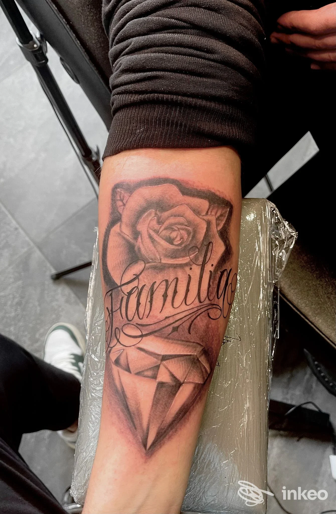 Primo piano di tatuaggio su avambraccio con rosa, scritta "familia" e diamante, realizzato da Skin ink tattoo and beauty potion a Montopoli in Val d'Arno.