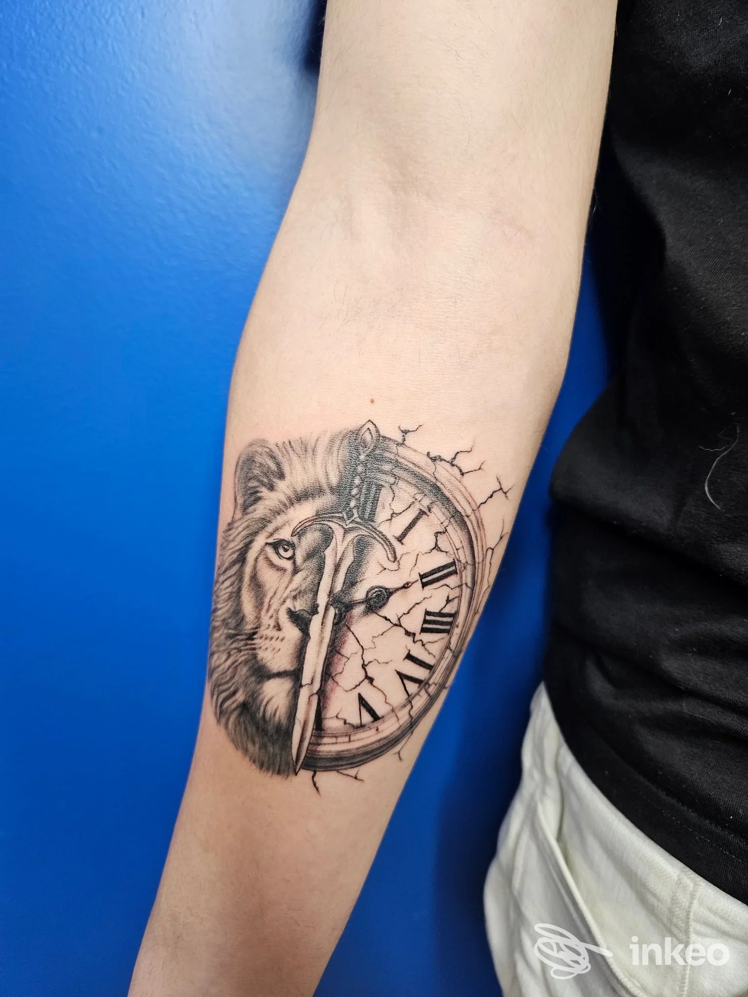 Tatuaggio in bianco e nero sull'avambraccio con leone e orologio rotto, foto fornita da Holo Ink Tattoo Studio, Sarzana.