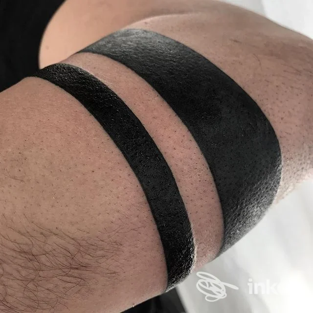 Due bande nere lucide stampate sulla pelle di un braccio, come tatuaggio. Nessun volto visibile, nessun testo o elemento di social media. Studio: Biumo Tattoo Club