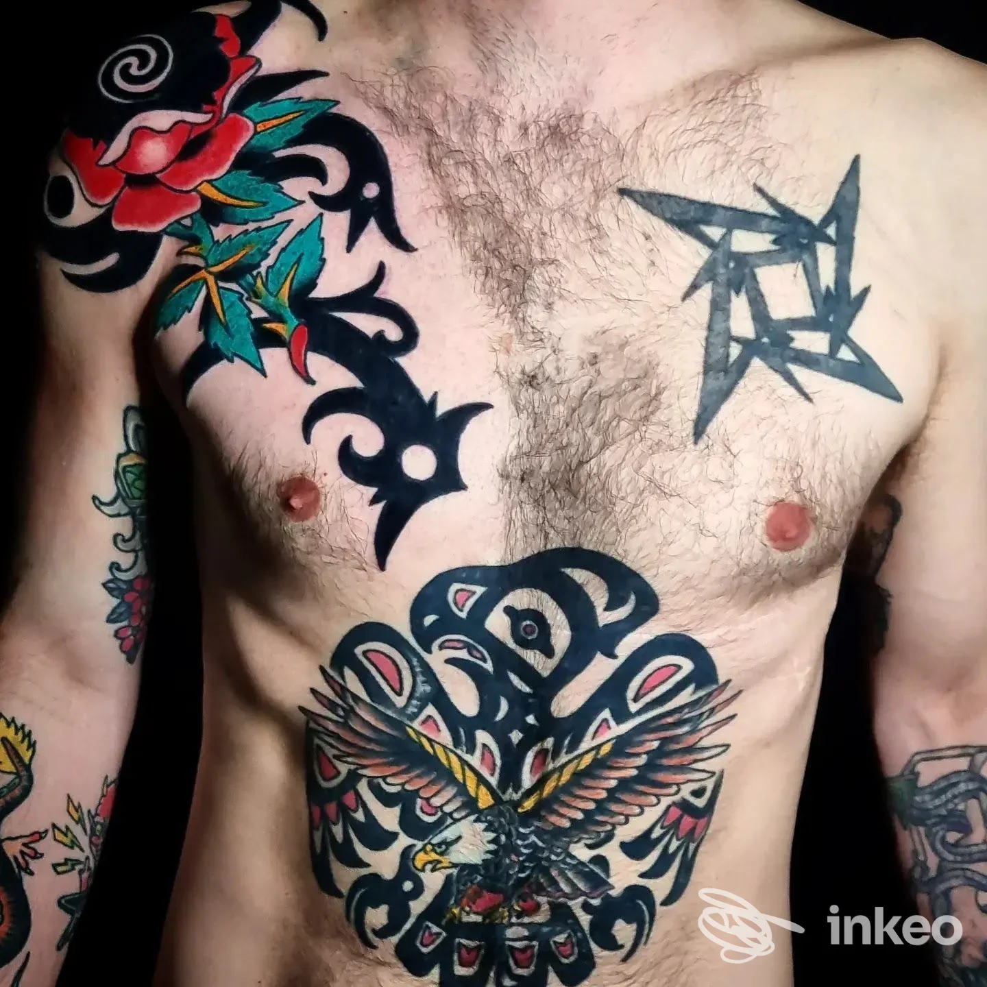 Primo piano del torace e braccio di un uomo, con tatuaggi visibili: tribale nero sul petto, motivo centrale a aquila colorata e decorazioni sul braccio sinistro, nessun volto presente.
