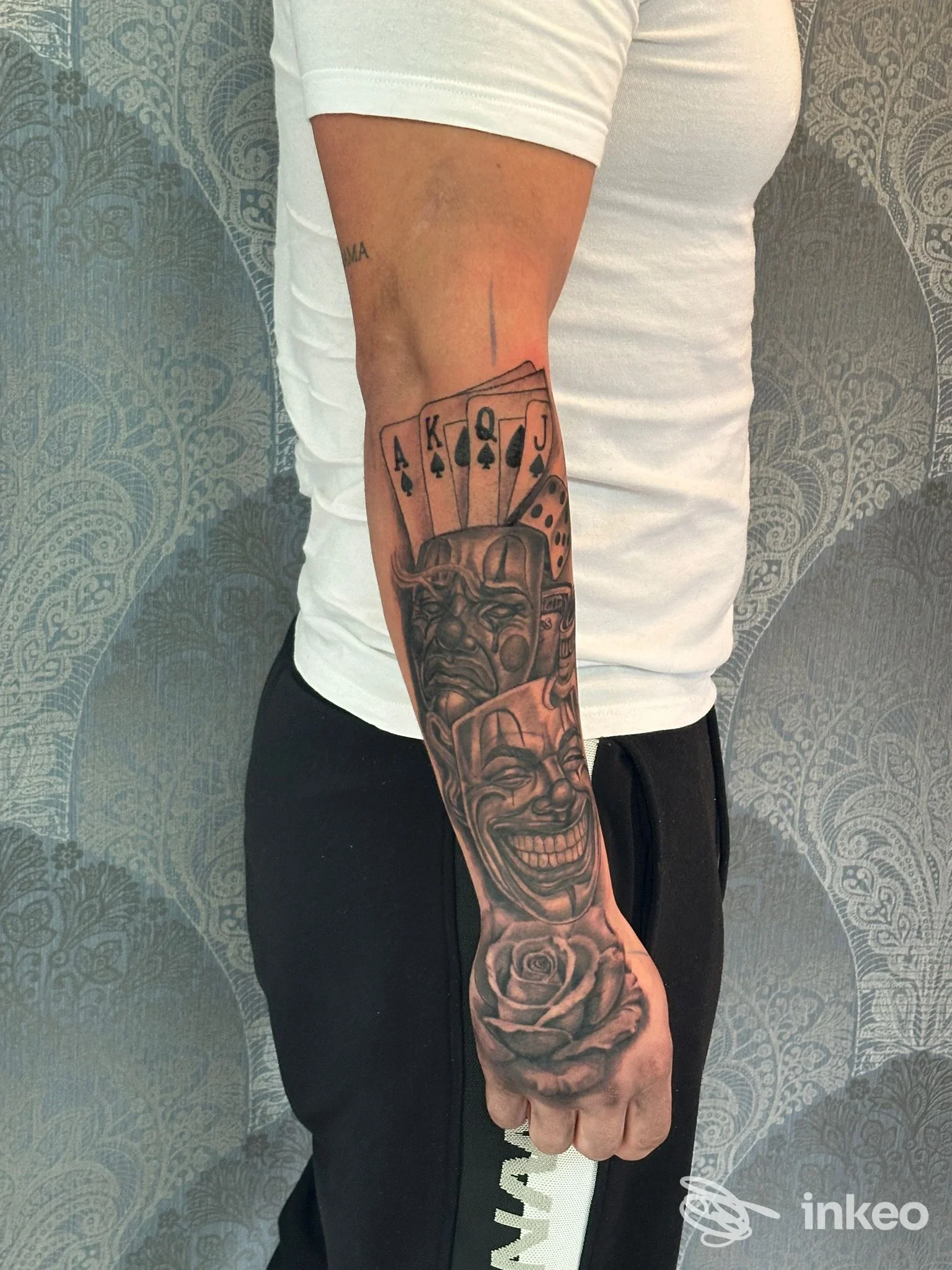 Tatuaggio black-and-grey su avambraccio e mano con carte, volti e rosa. Black Realism Tattoo, Altivole.