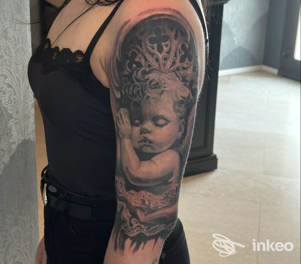 Grande tatuaggio realistico in bianco e nero di un bambino addormentato sul braccio, foto fornita da Black Realism Tattoo, Altivole.