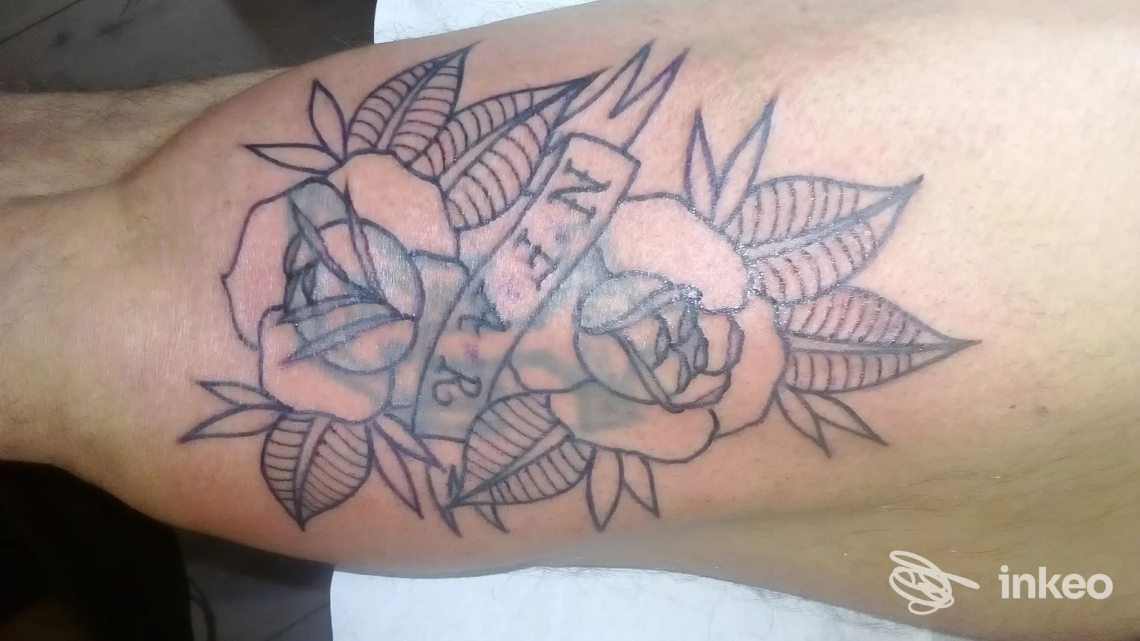 Tattoo visibile sull'avambraccio: rose intrecciate con nastro, linee nette e ombreggiature leggere. Nessun volto o contenuto di interfaccia social visibile.