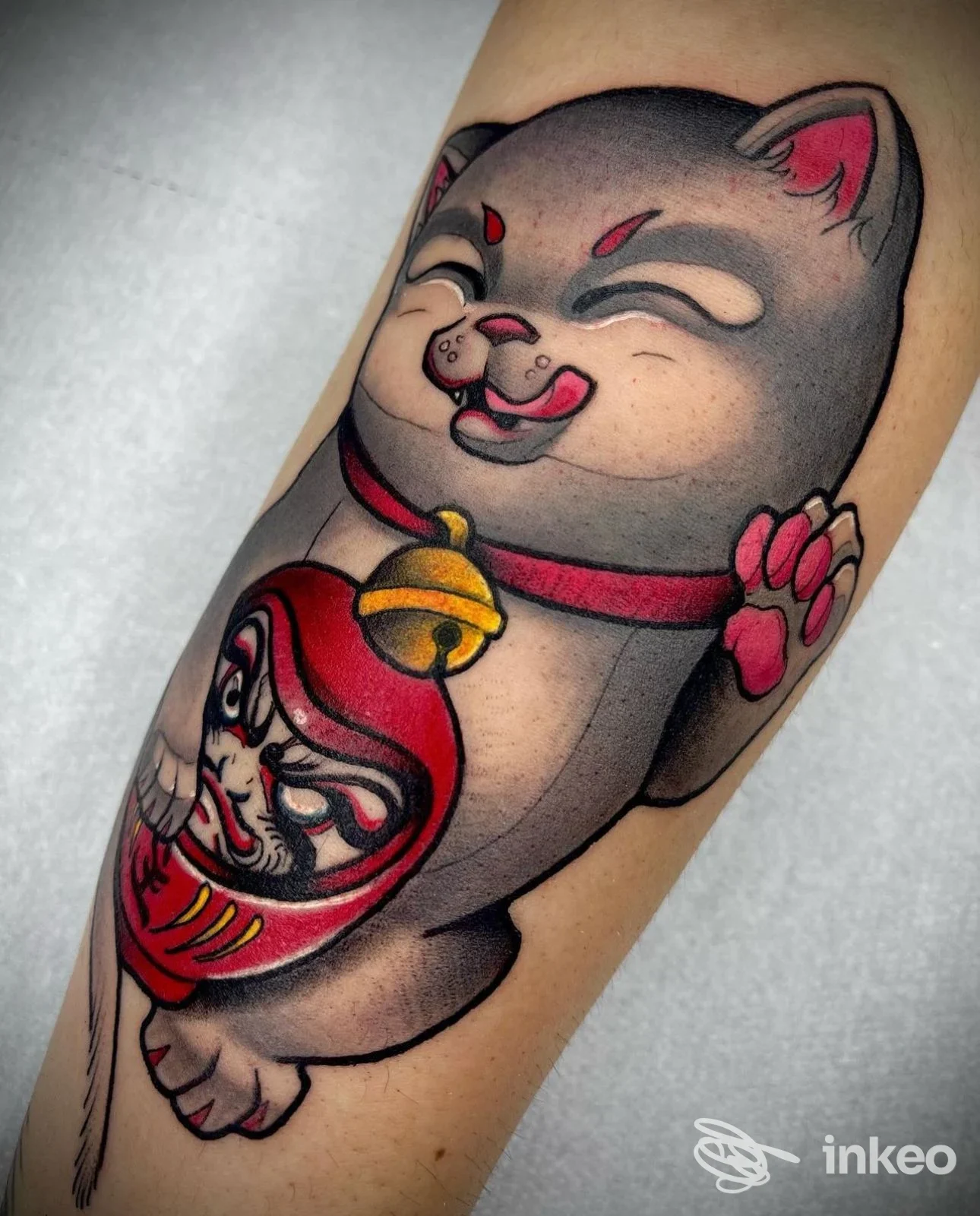 Tatuaggio colorato a Verona: maneki-neko che regge un daruma, realizzato da Ink Inside Tattoo Studio sull'avambraccio.