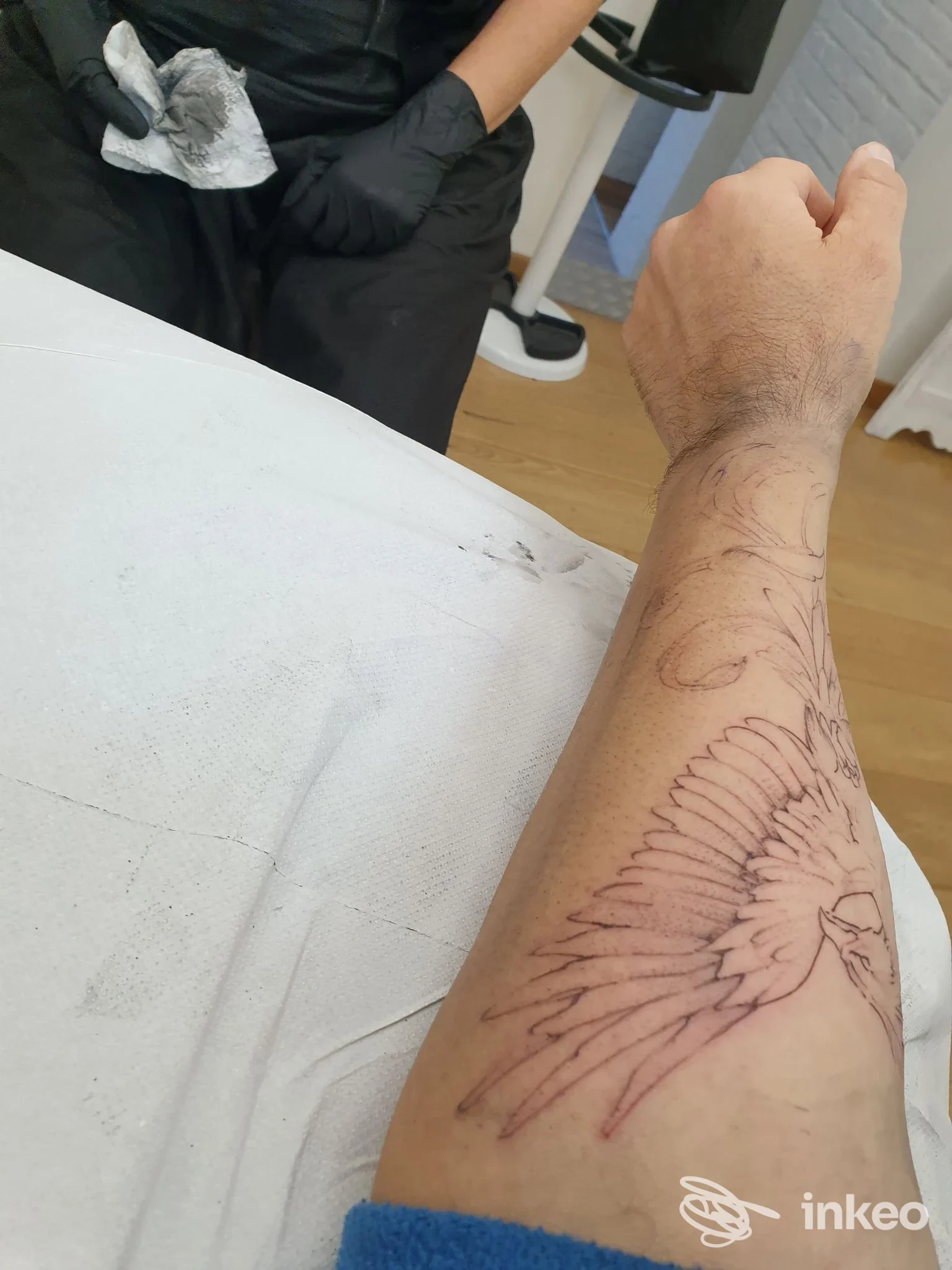 Avambraccio con bozza di tatuaggio a forma di ali su lettino, operatore con guanti visibili — Lo Ro' tattoo studio, Galliera Veneta.