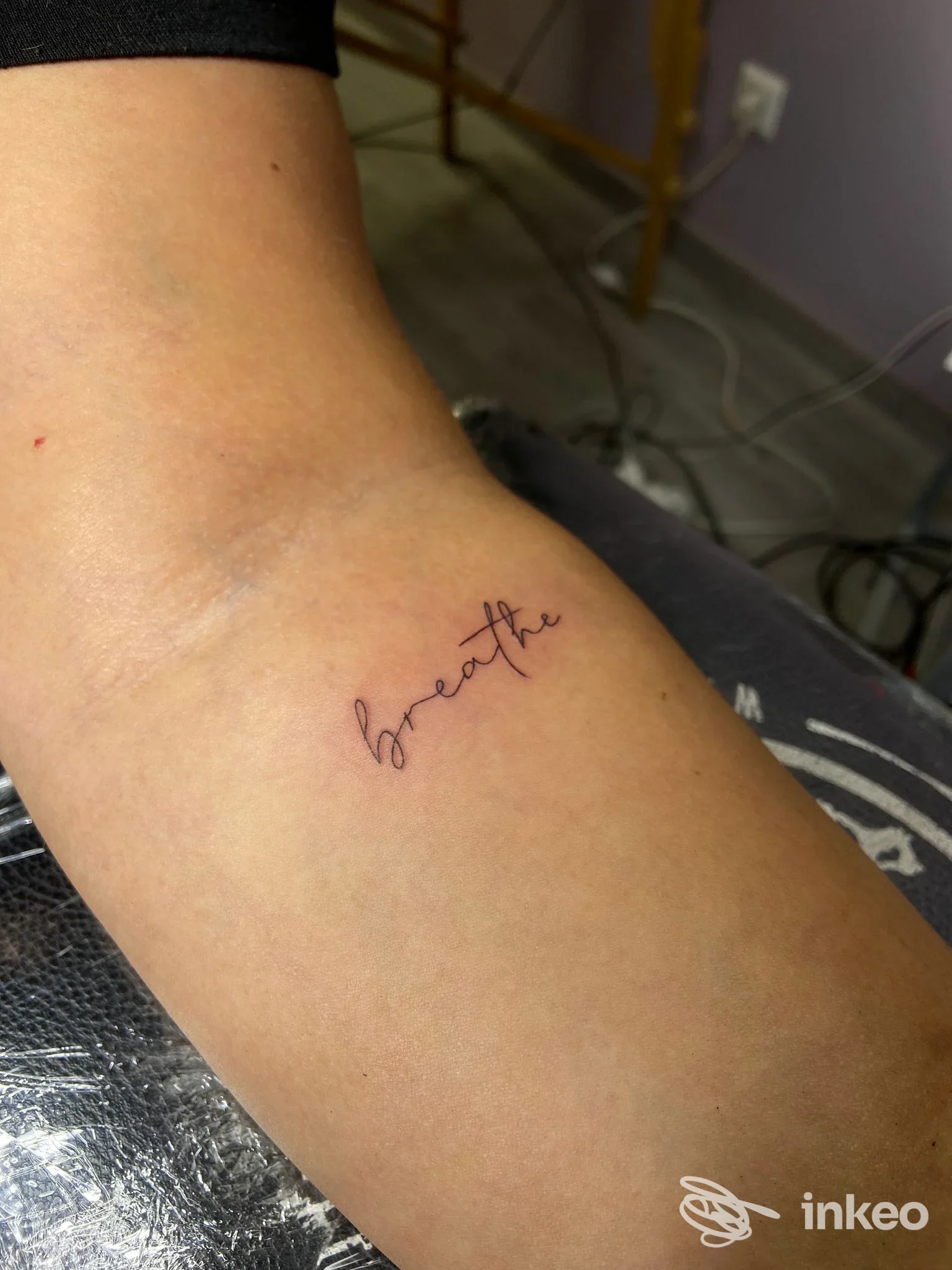 Tattoo sulla pelle di una coscia laterale: piccola scritta in corsivo 'breathe' visibile nel dettaglio.