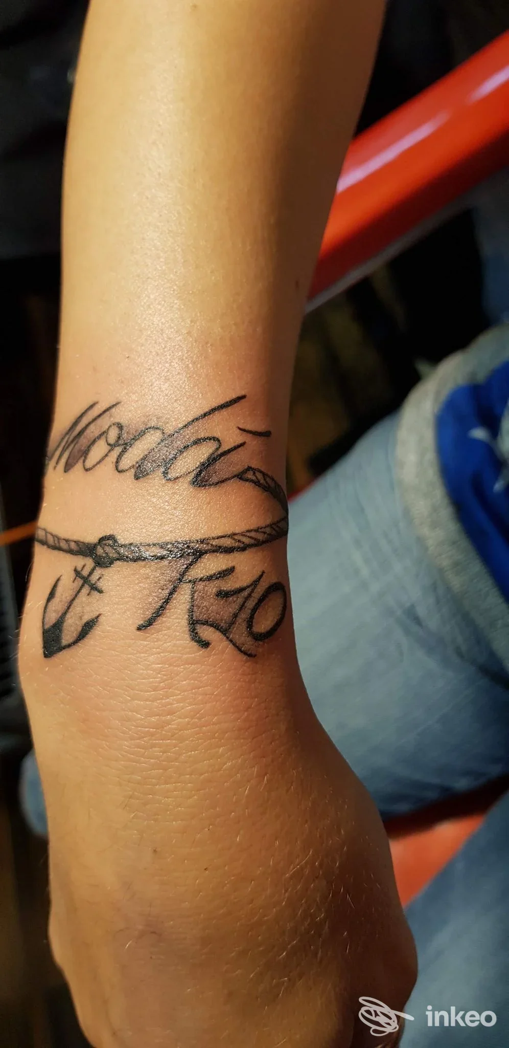Tattoo visibile sul braccio con testo in stile corsivo intrecciato a una bordatura simile a una corda, realizzato sulla pelle.