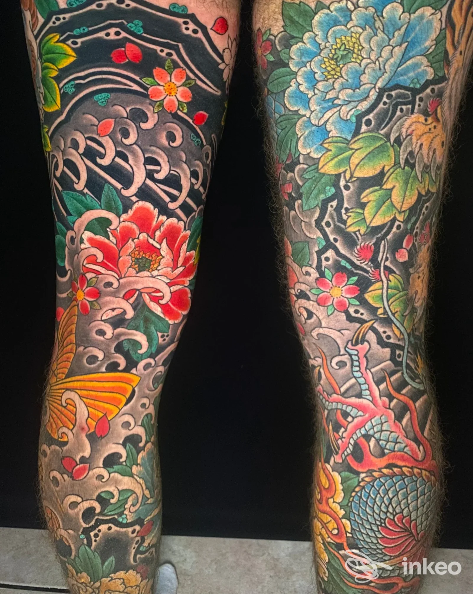 Due polpacci tatuati con ampi motivi floreali, onde e decorazioni colorate in stile tradizionale; Tattoo River, Vicenza.