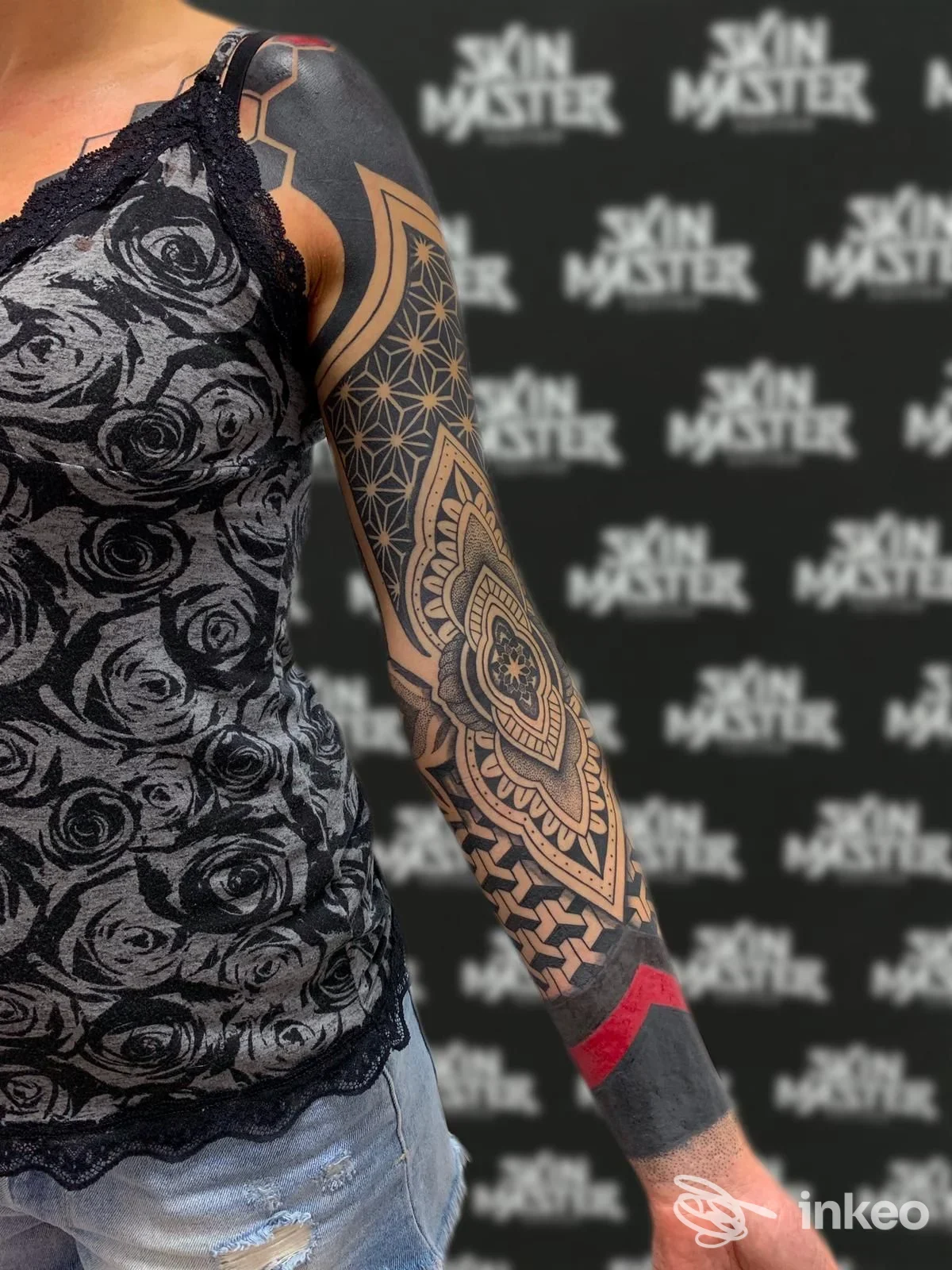 Braccio sinistro con tatuaggio geometrico mandala lungo l’avambraccio, tessuto a motivo floreale scuro, sfondo con logo Skin Master Tattoo.