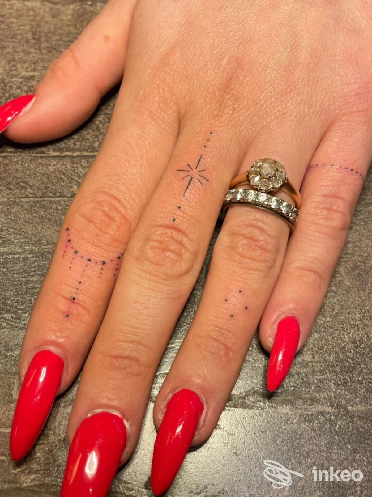 Mano con micro-tatuaggi puntinati e una piccola stella sulle dita, unghie rosse lucide; Nebula Tattoo Studio, Borgo A Buggiano.
