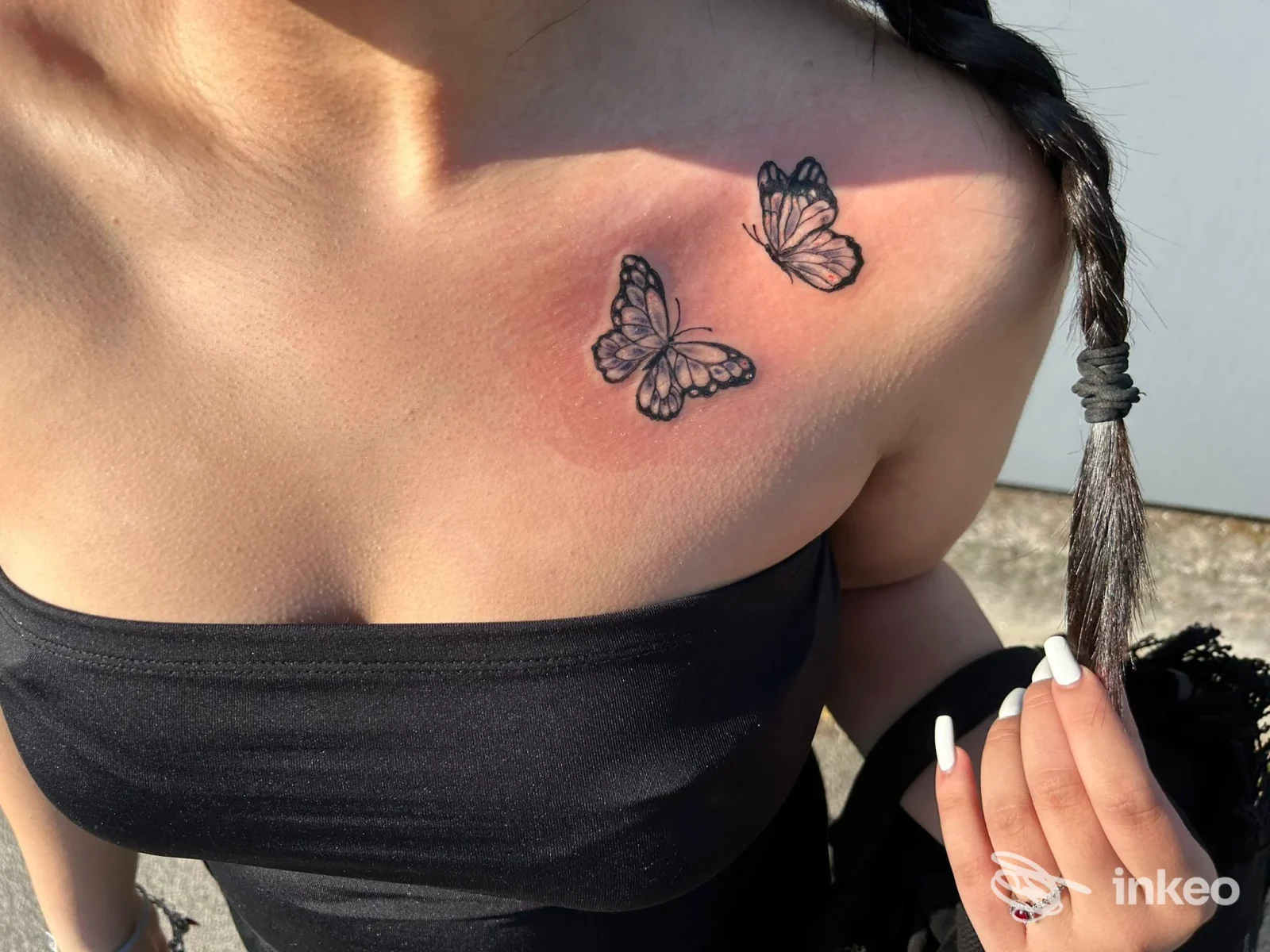 Due piccoli tatuaggi a forma di farfalla in nero sulla clavicola sinistra, foto scattata nello studio Eros Body Art a Noventana.