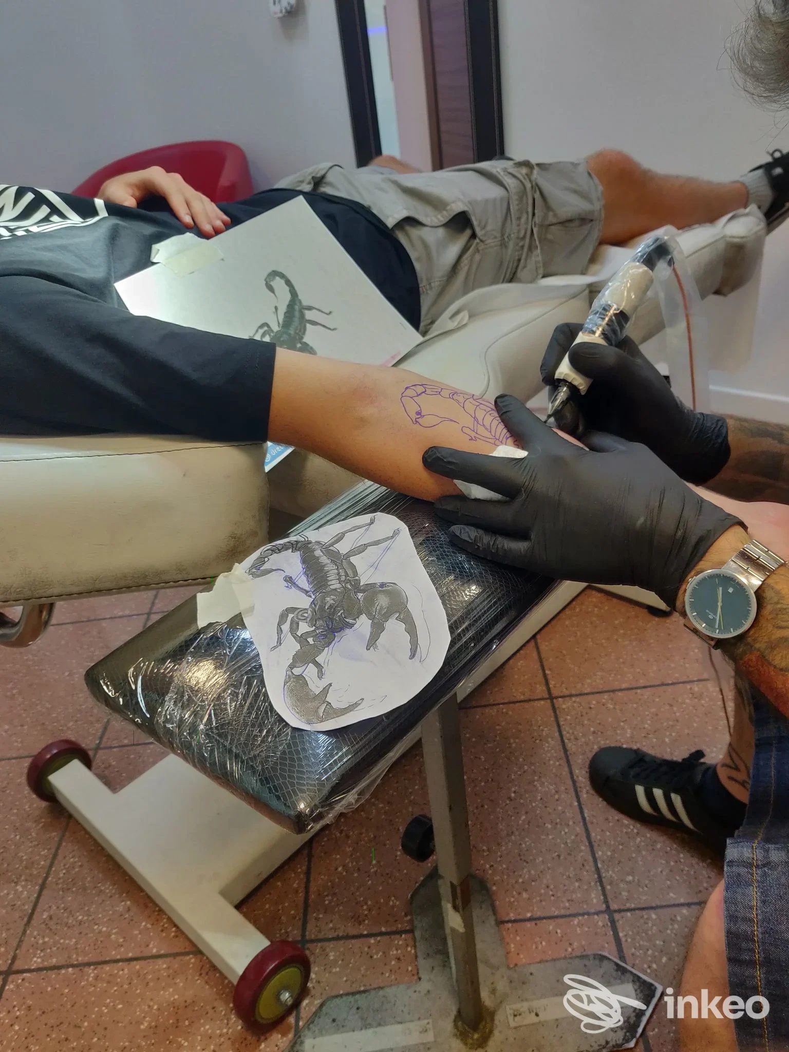 Tatuatore al lavoro su avambraccio con disegno di scorpione come riferimento, immagine dallo studio Eros Body Art Di Belluco Eros a Noventana.