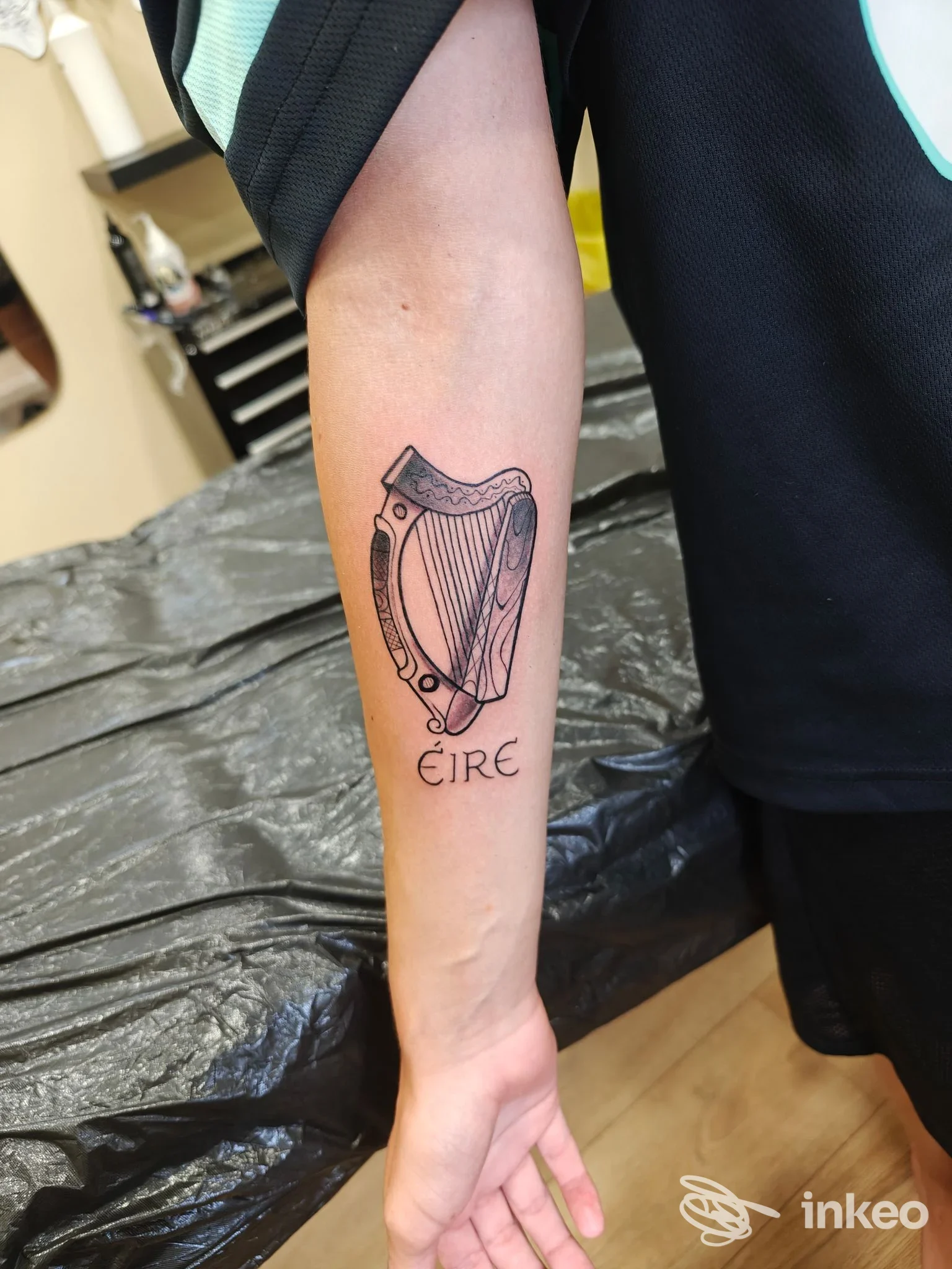 Tatuaggio di arpa stilizzata con la scritta 'Éire' sull'avambraccio, realizzato da Black Sunset Tattoo & Piercing Studio a Bibione.