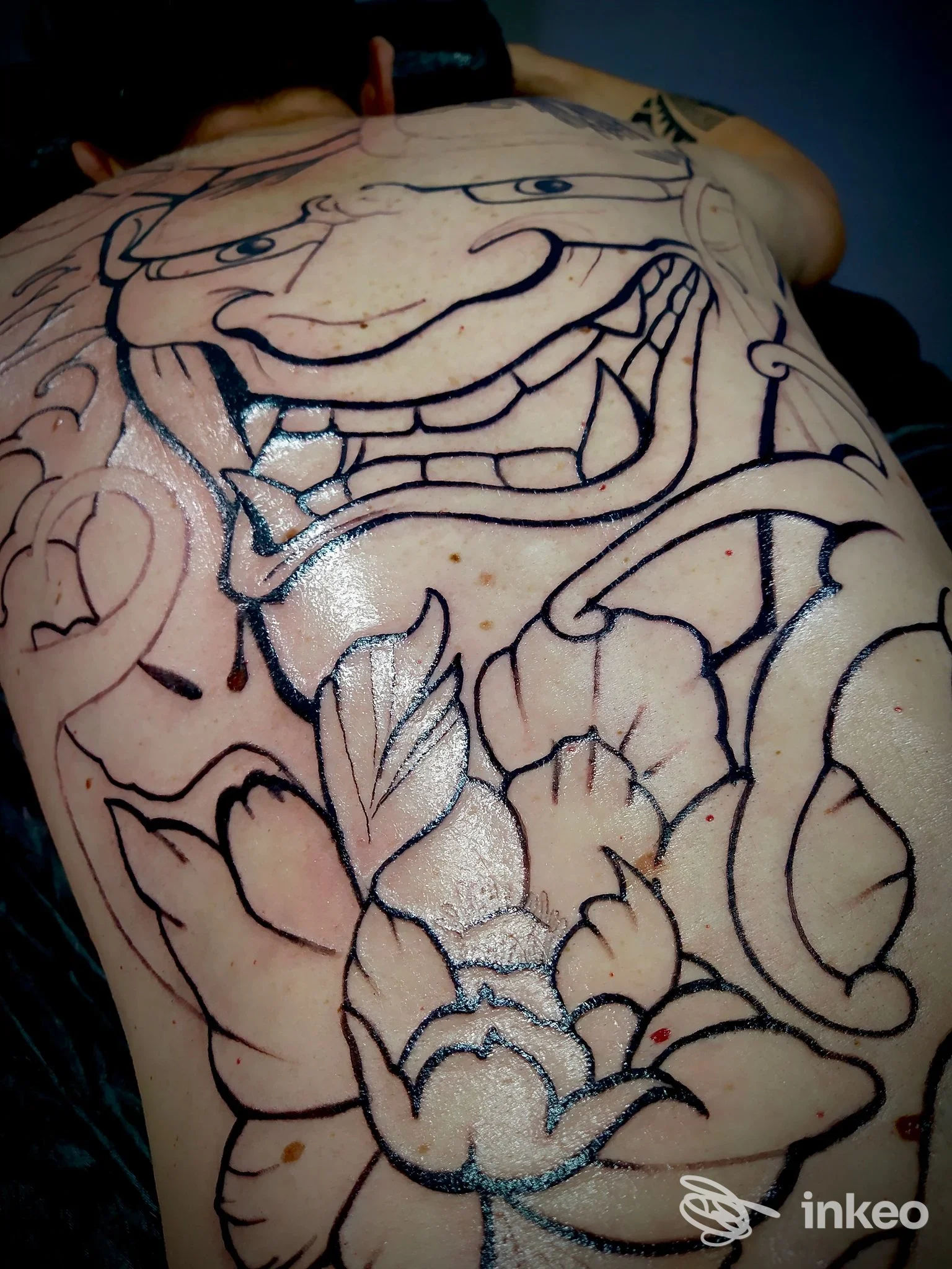 Tatuaggio grande in lavorazione sulla schiena con motivi floreali e volto stilizzato, Riviera Tattoo House, Oriago.