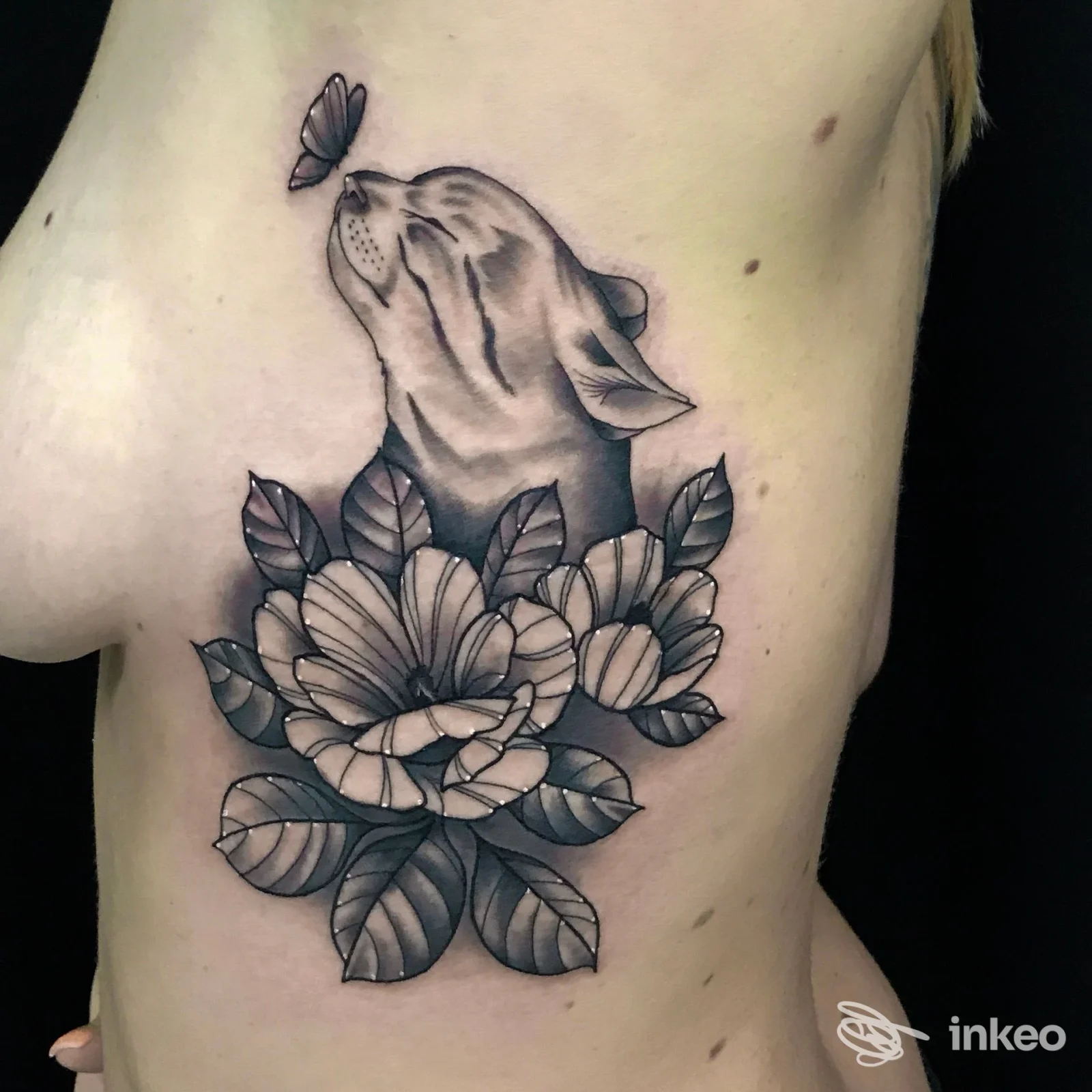 Tatuaggio in bianco e nero sul fianco con gatto stilizzato, fiori e foglie; lavoro fotografato presso Tattoo Boutique, Colfosco.