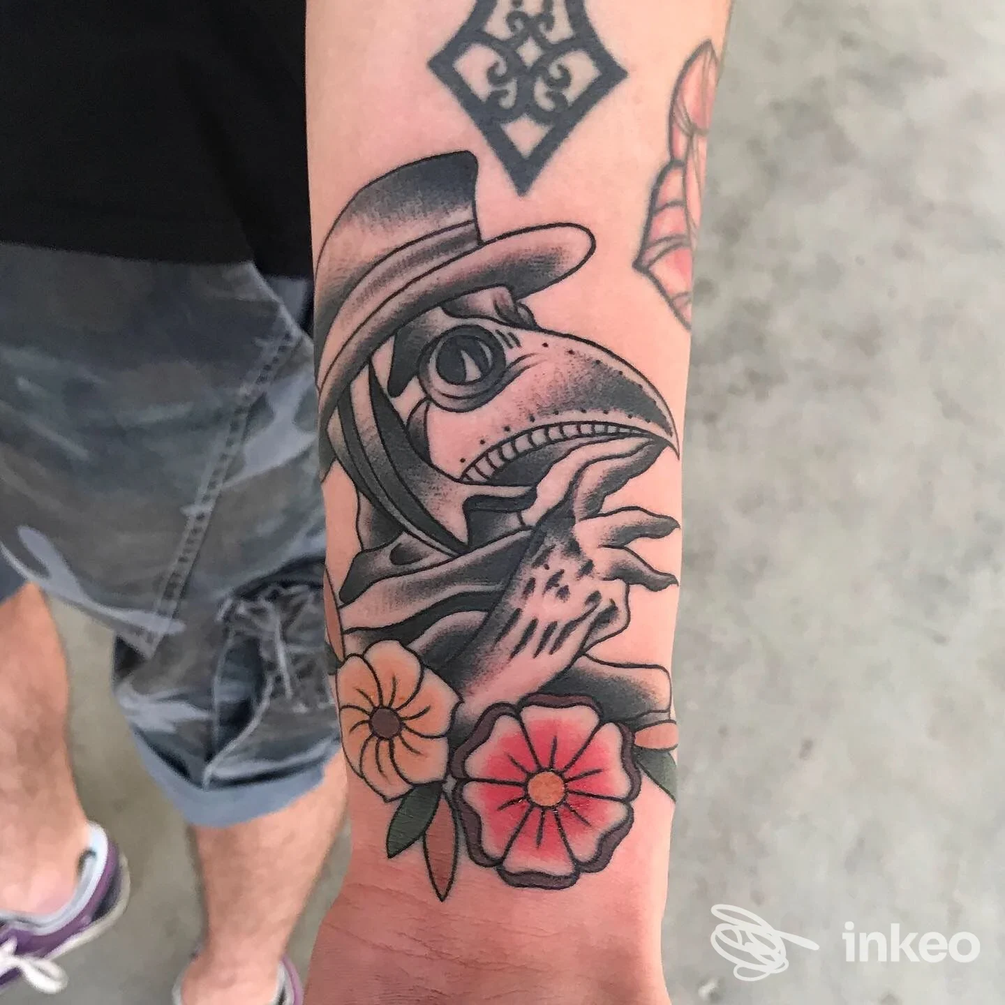Tatuaggio su avambraccio con medico della peste in bianco e nero e fiori colorati, immagine fornita da Tattoo Boutique, Colfosco.