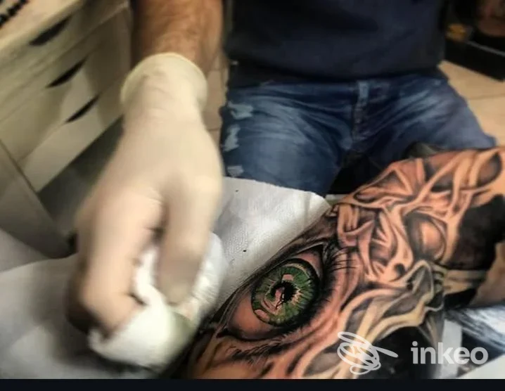 Primo piano di un tatuaggio realistico a forma di occhio su avambraccio, operatore con guanto che pulisce. Giotattoo, Bagnaia.
