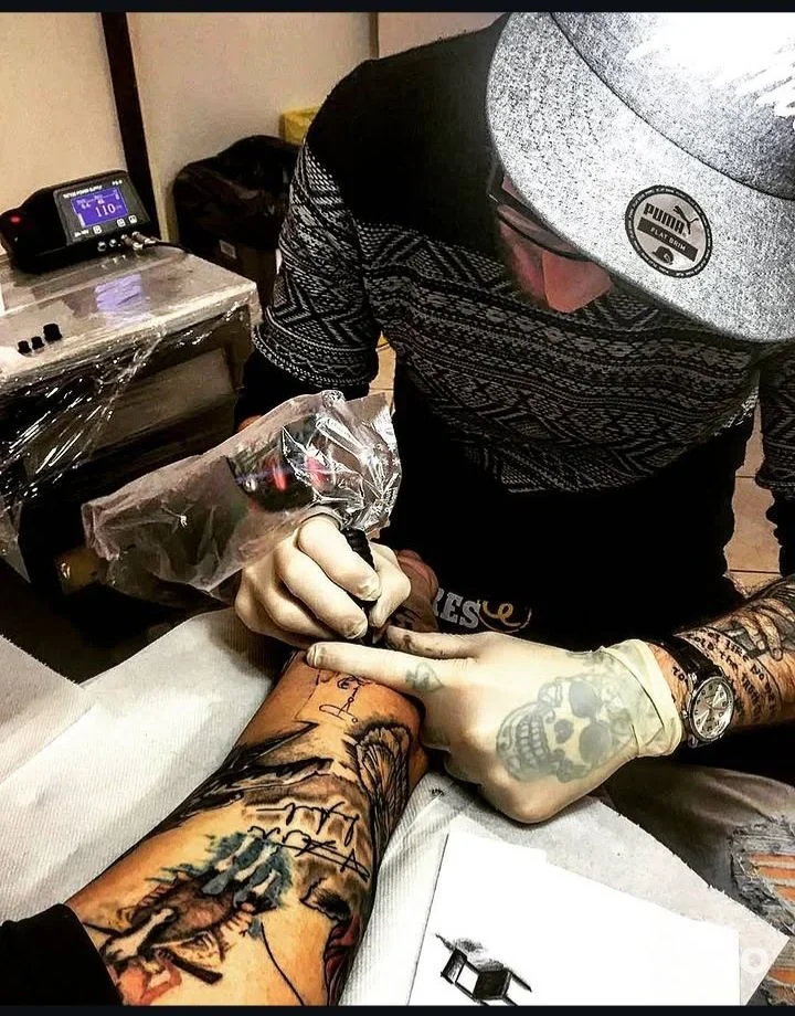 Artista di Giotattoo (Bagnaia) mentre tinge un avambraccio tatuato in studio, mano guantata e postazione visibile.