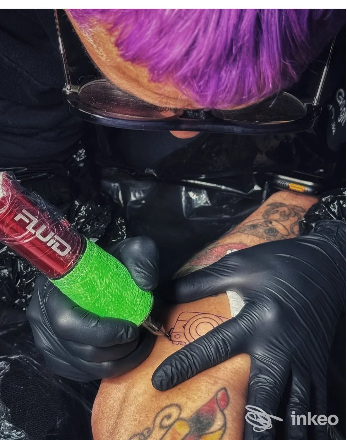 Tatuatore al lavoro su avambraccio con macchina avvolta in nastro verde, Negozio di tatuaggi, Pagliare del Tronto.