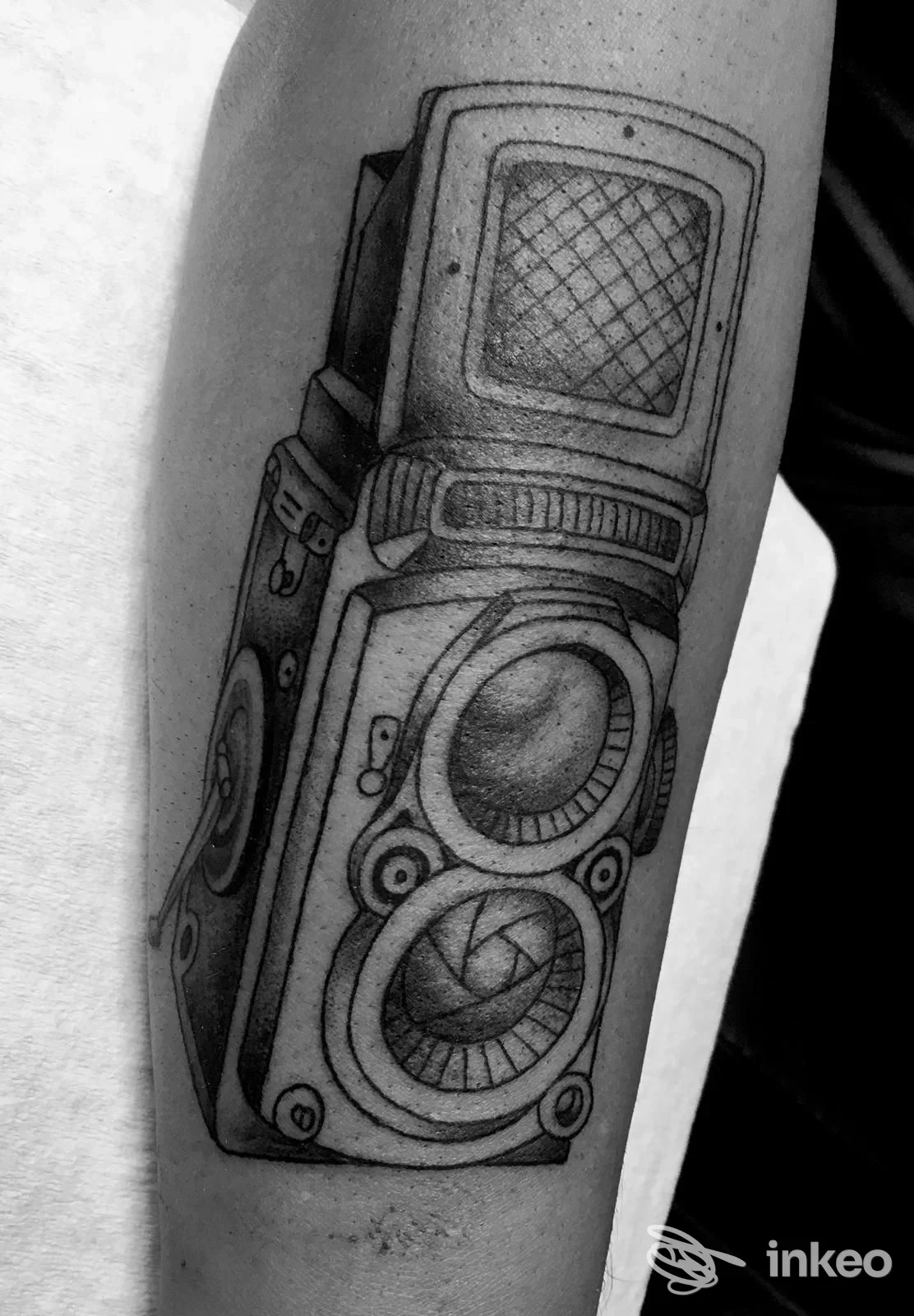 Tatuaggio realistico in bianco e nero di una macchina fotografica sul davanti dell'avambraccio, SONOS TATTOO ART, Arbatax.