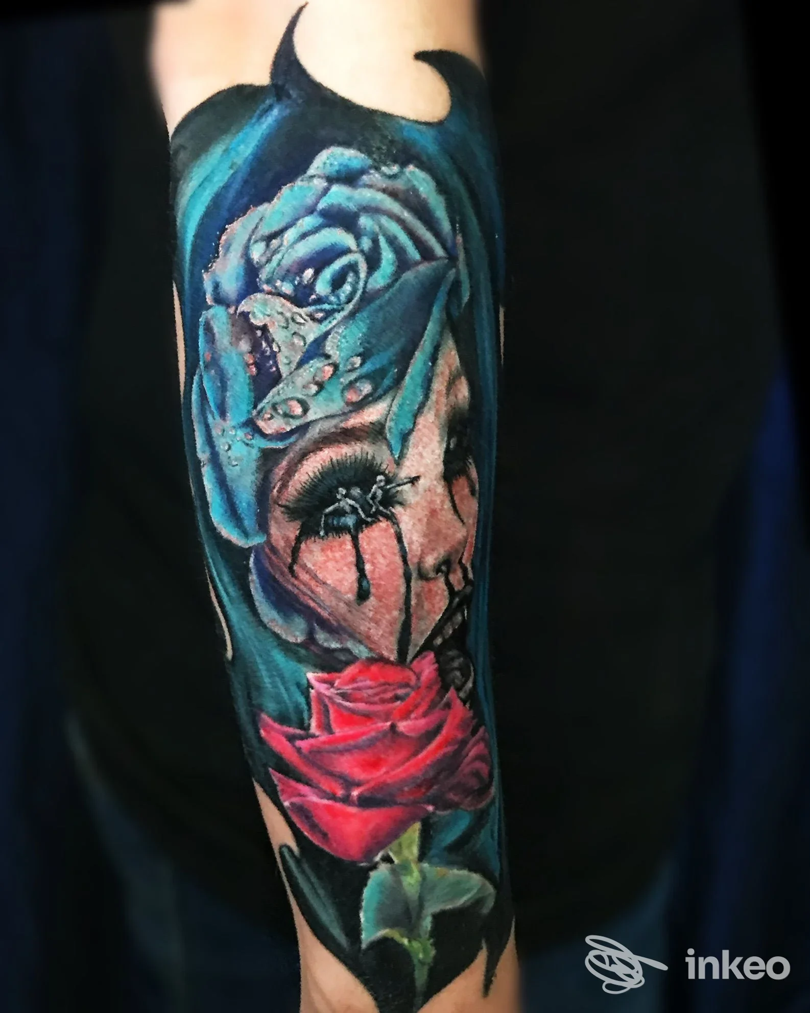 Tatuaggio realistico e colorato su avambraccio con grandi rose rosse e blu e un elemento cranico fotografato per Cat Ink Tattoo Art Studio, Latina Scalo.
