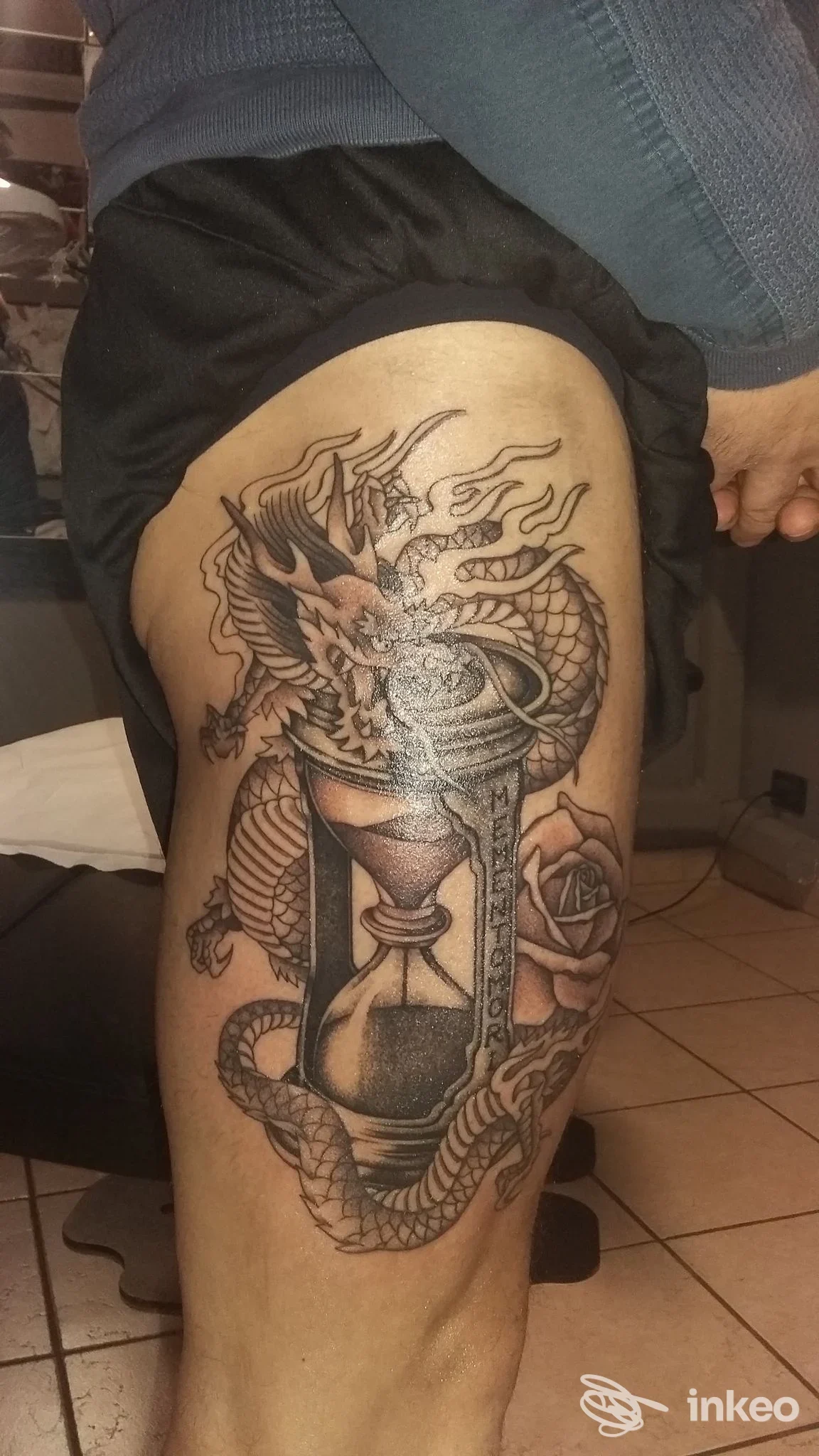 Grande tatuaggio su coscia con drago avvolto attorno a una clessidra e una rosa, foto fornita da Chianti Ink, Tavarnelle Val di Pesa.