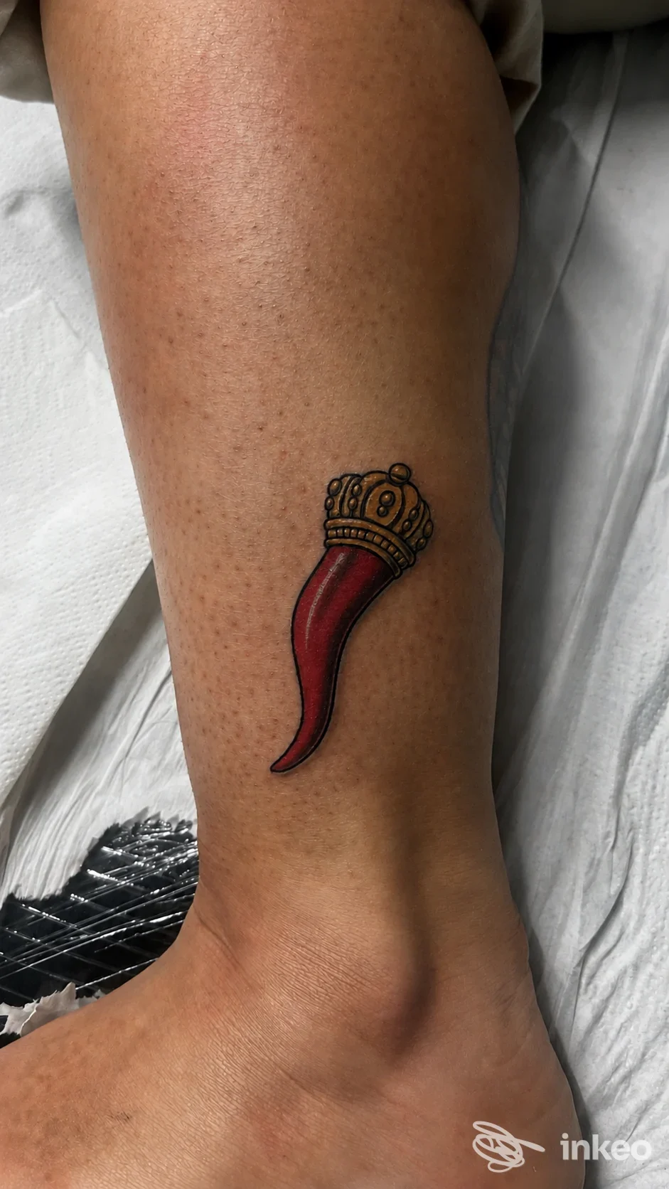 Tatuaggio a Napoli presso tattoo store: cornetto rosso con corona dorata sulla parte inferiore della gamba vicino alla caviglia.