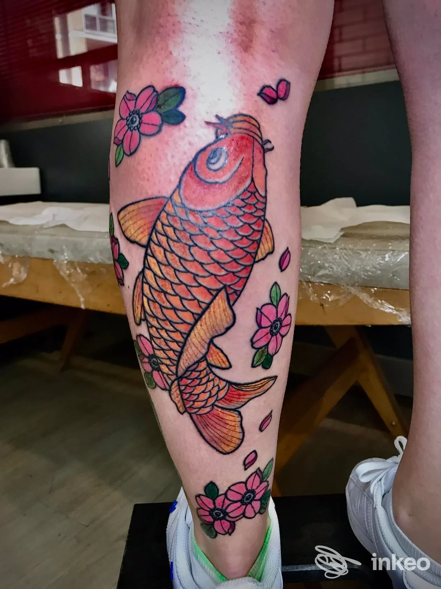 Koi arancione e fiori tatuati sul polpaccio, dettagli nitidi e contorni netti; opera di Alex Sabattini Tattoo a Bologna.