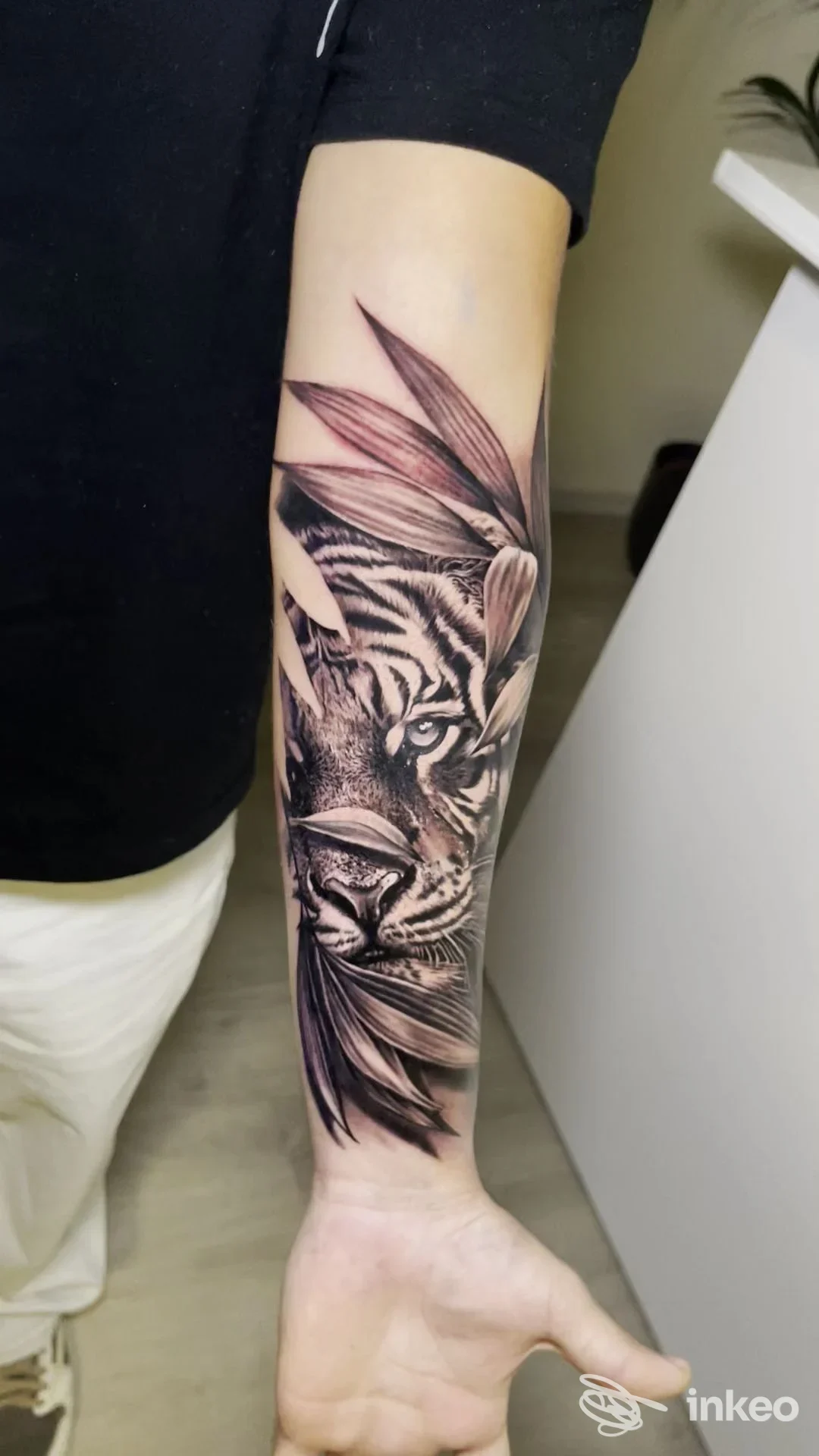 Tatuaggio realistico di tigre in bianco e nero sull’avambraccio sinistro, con dettagli sull’occhio e la pelliccia, accompagnato da elementi decorativi.