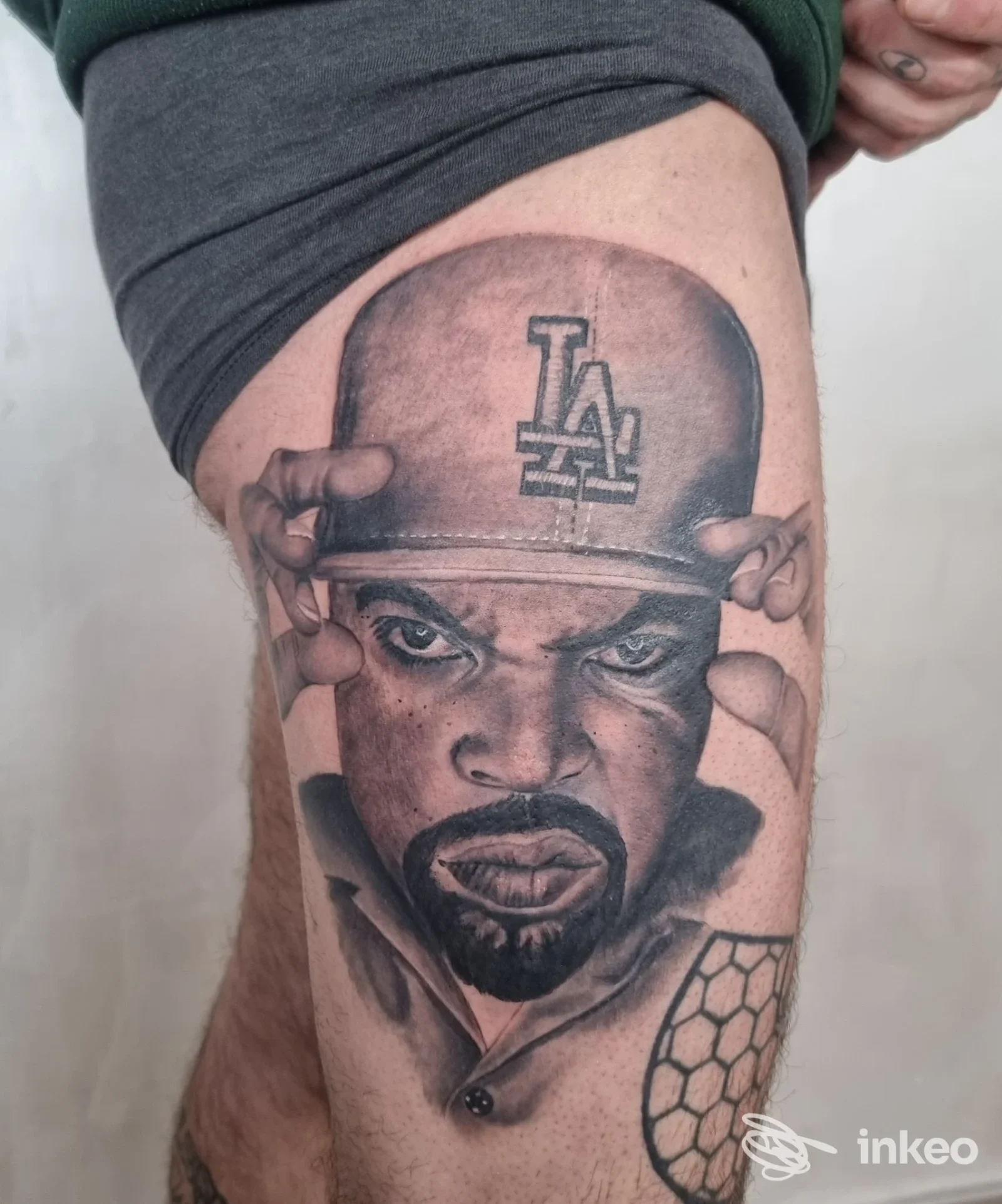 Ritratto realistico tatuato sulla coscia con cappello LA, lavoro eseguito da Tardox Tattoo a Salerno.