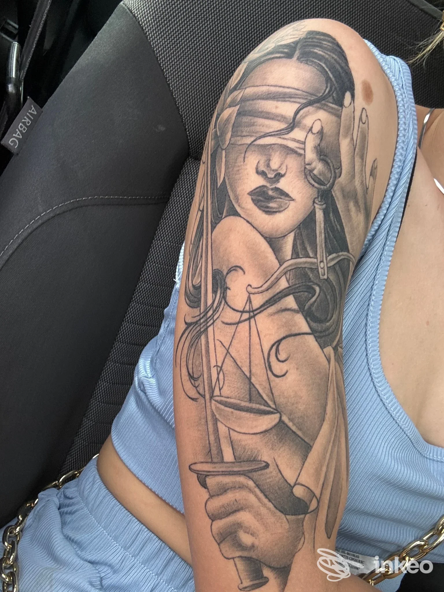 Tattoo sul braccio di una persona: una donna stilizzata con elementi decorativi come bilance e lama, in tonalità scure su pelle chiara. Studio Ser.ink Tattoo Studio.