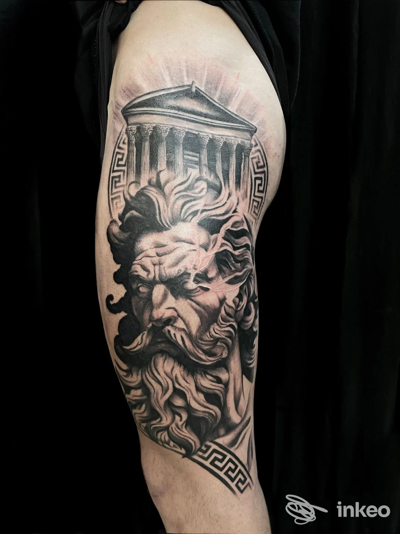 Tattoo in bianco e nero sull'avambraccio: volto barbuto con cappello classico e colonne, ornamenti geometrici ai bordi.