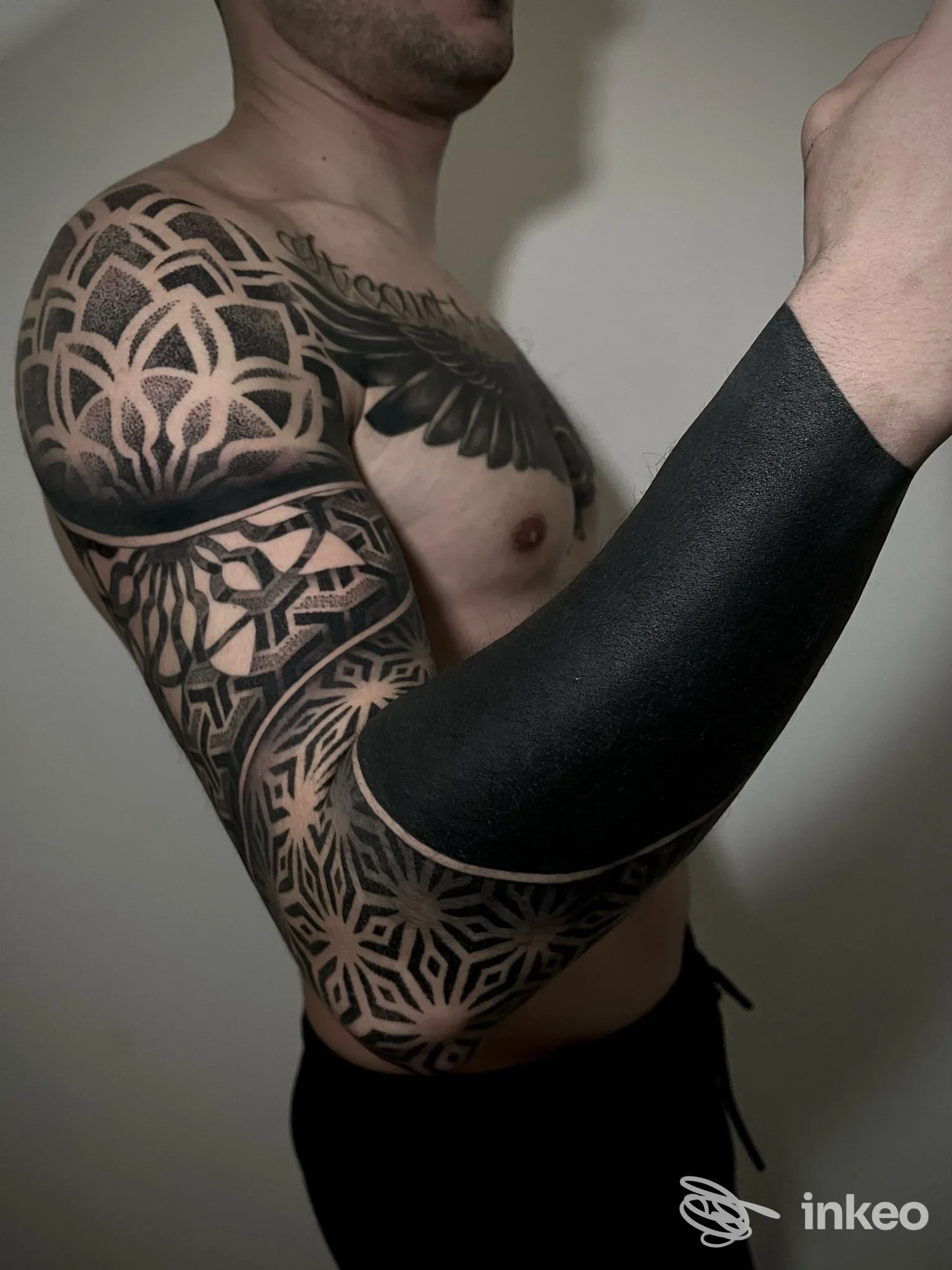 Tattoo geometrico a maniche lunghe su braccio sinistro, visibile su una parte del torace del modello maschile.