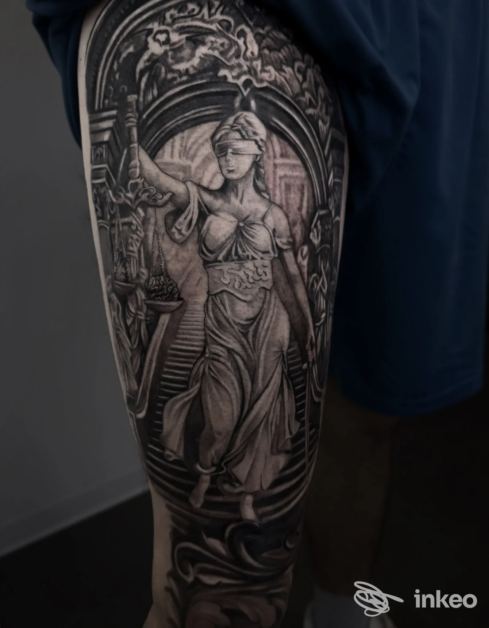 Tattoo in bianco e nero su gamba di una figura femminile classica incorniciata da archi decorativi, realizzazione visibile sulla pelle.