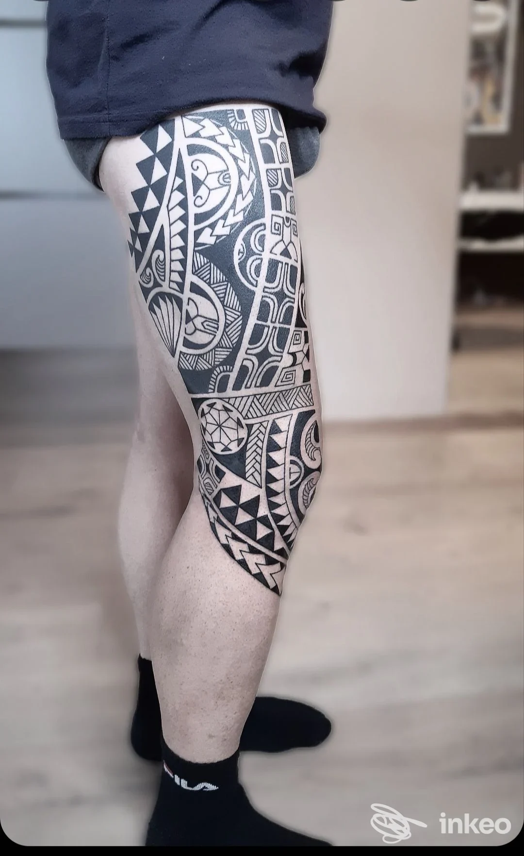 Tattoo geometrico nero su gamba destra: motivi triangolari e cerchi che coprono gran parte della tibia e della coscia.