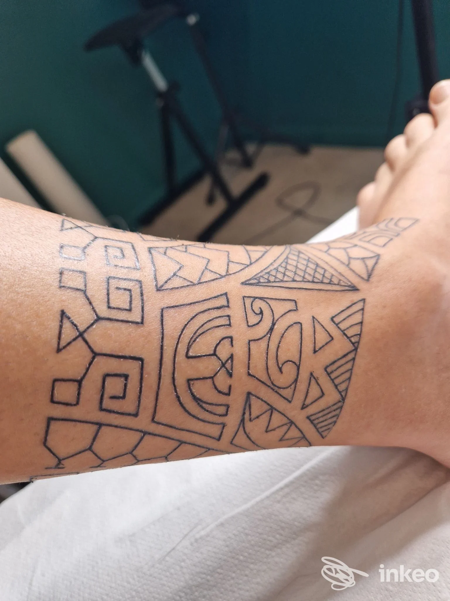 Tattoo geometrico su avambraccio, linee nere su pelle chiara, disegno continuo senza testo né loghi visibili, scatto singolo.