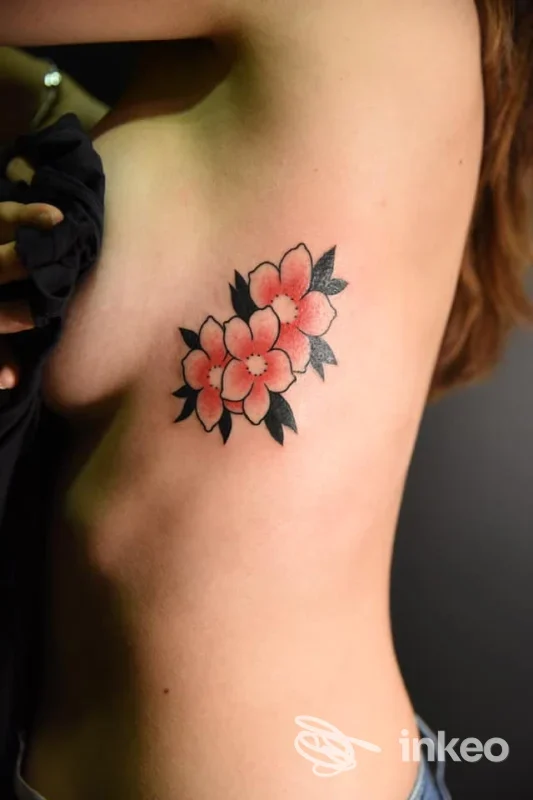Tattoo floreale rosa con foglie nere sulla pelle della sopraascella sinistra di una persona, illuminazione mirata e linee nette.