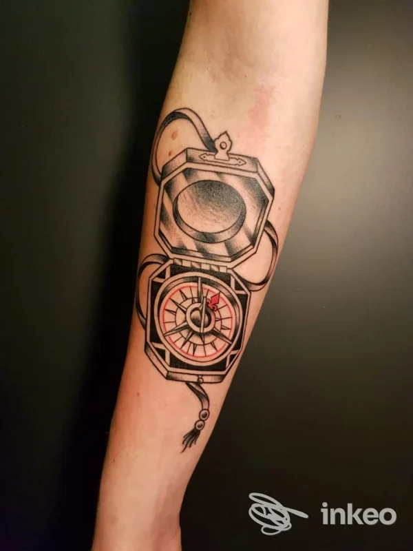Tatuaggio sul braccio raffigurante un orologio/ bussola in stile linework, molto definito, con dettagli neri e piccole punte rosse, realizzato sulla pelle; eseguito da Mt Tattoo Studio a Cremeno.