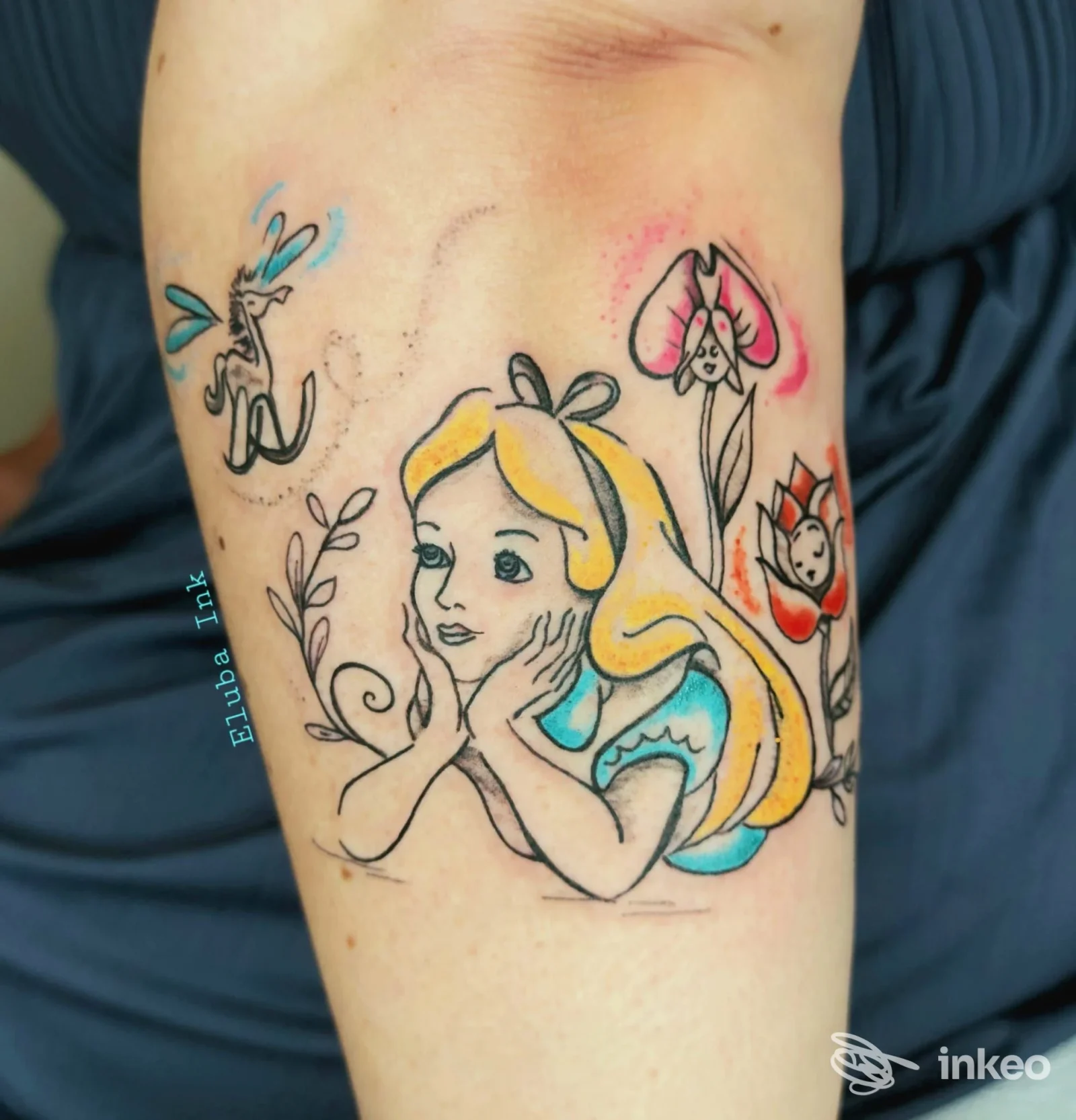Tatuaggio colorato su braccio raffigurante una ragazza stilizzata con capelli biondi e fiori, realizzazione su pelle visibile senza volto umano completo.
