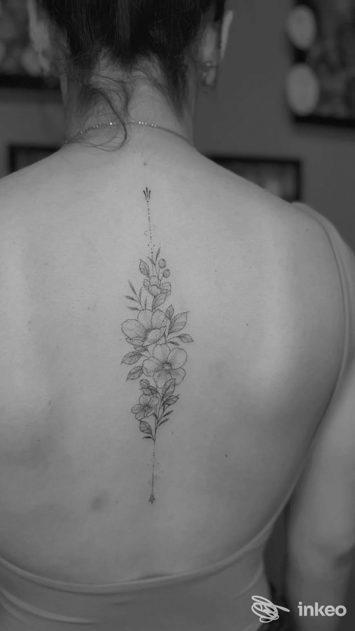 Particolare di una schiena nuda con un tatuaggio verticale di fiori lungo la colonna vertebrale, nessun volto visibile, luce neutra, stile sobrio.